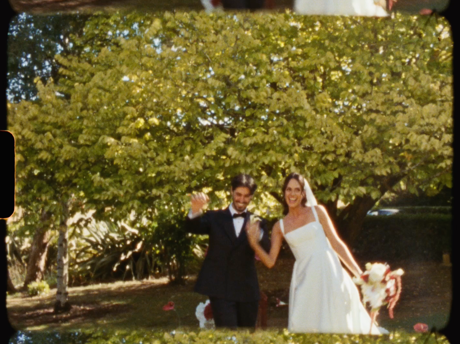 Happy bride and groom posing playfully with a dog in a lush green garden after their wedding.