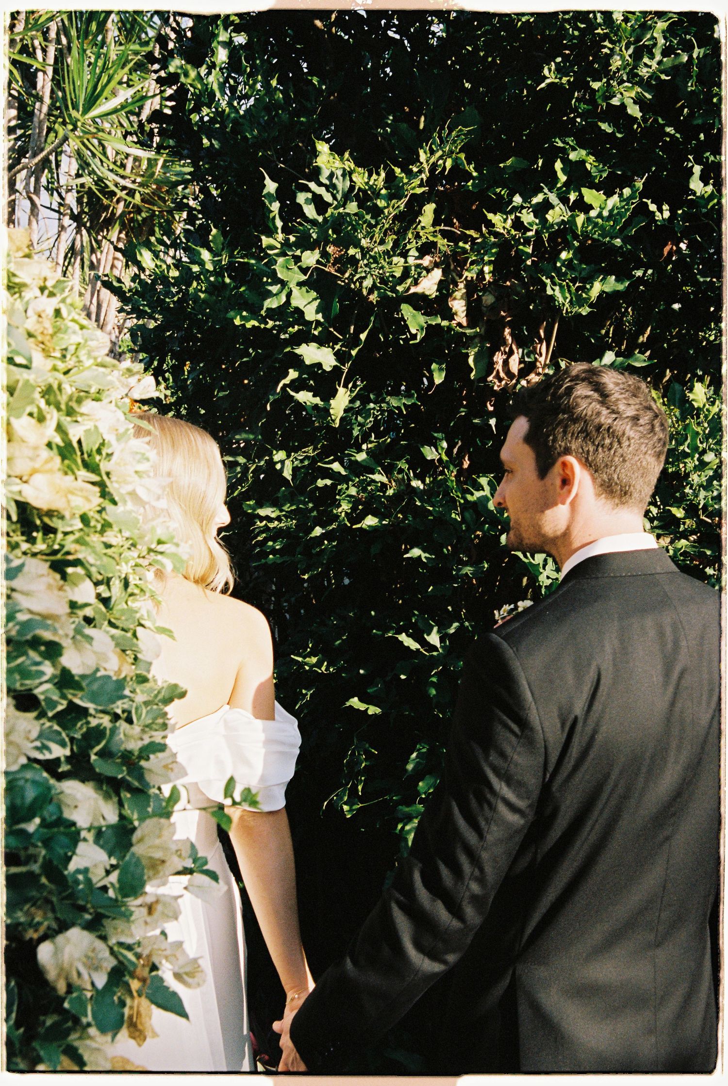 Bride and groom standing together before a lush green ivy wall during outdoor wedding ceremony.