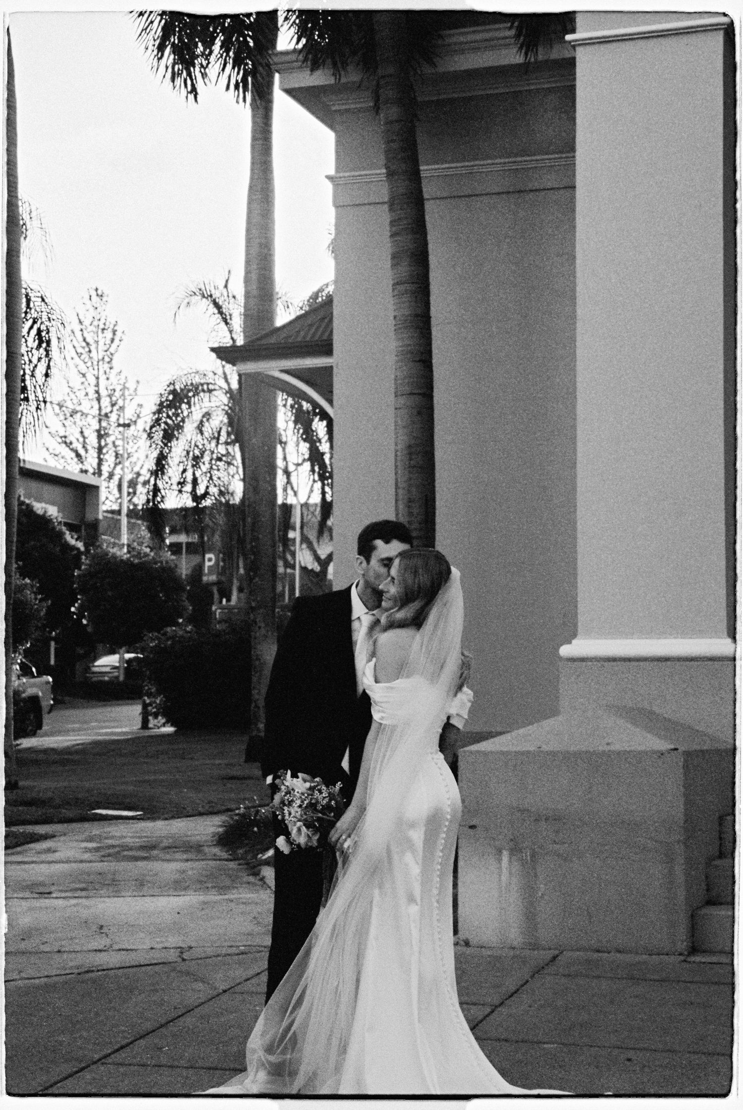A bride and groom share a kiss outside a grand building on their wedding day.