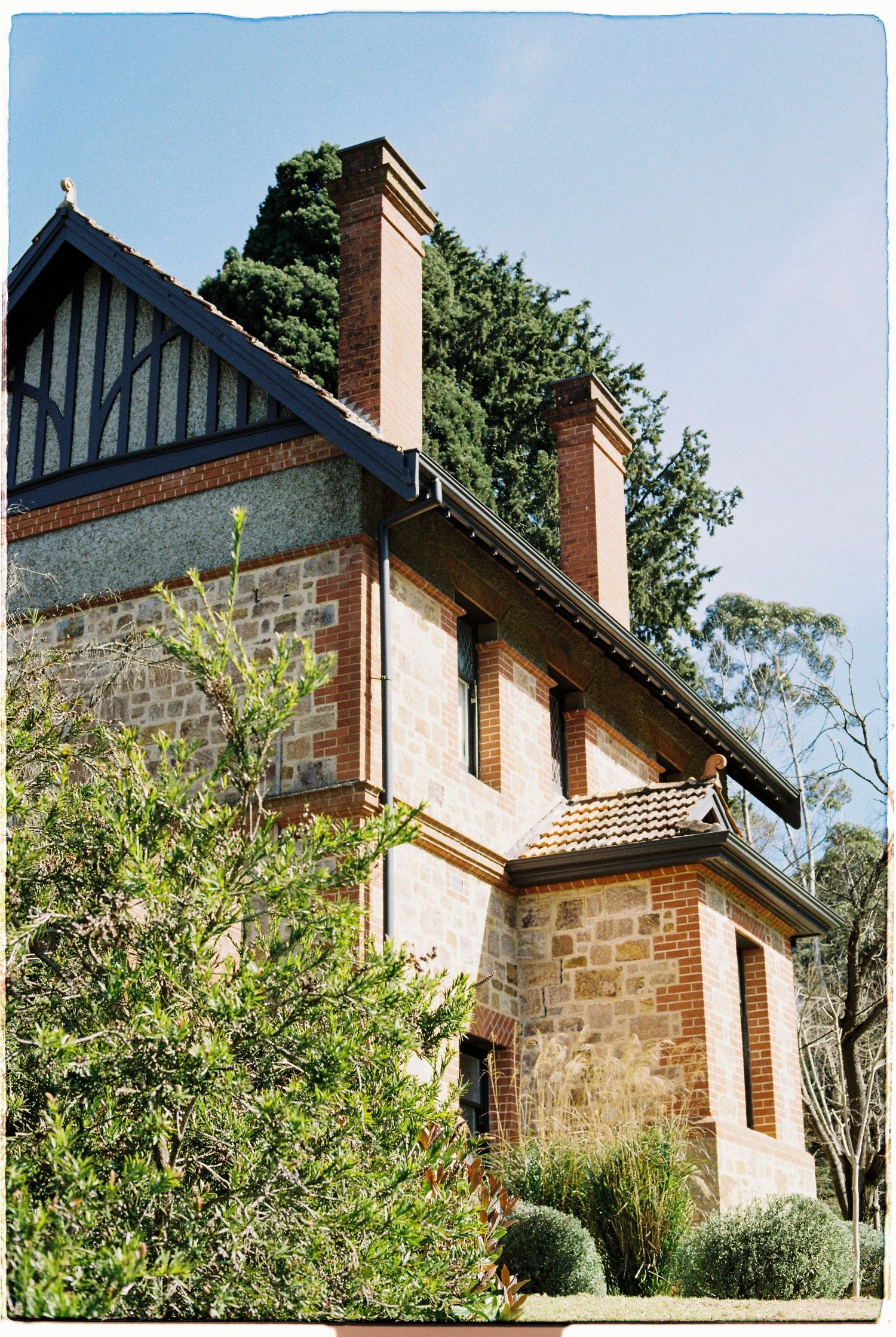Historic stone and brick building with tall chimneys and timber gable detail against blue sky.