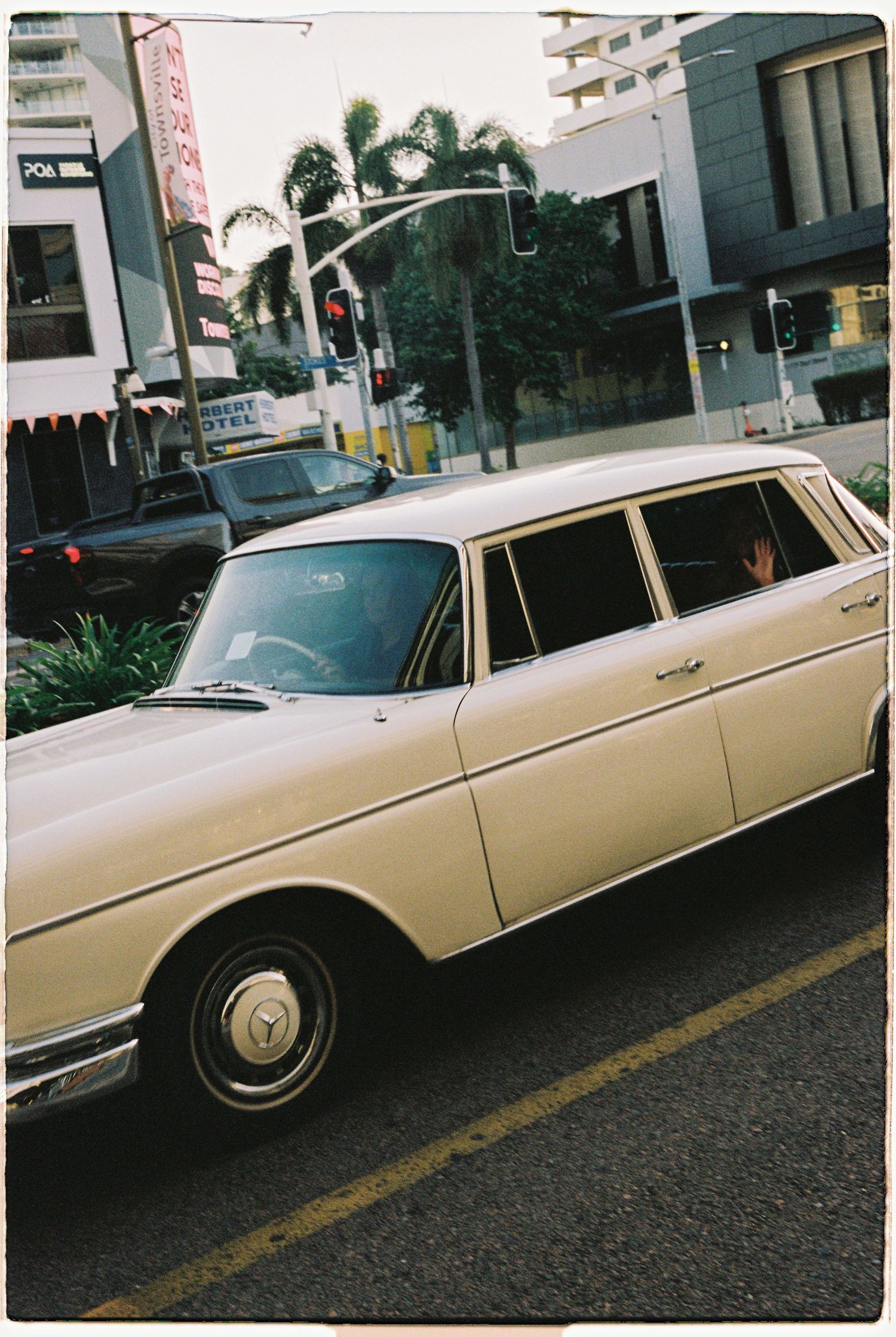 Classic cream vintage Mercedes-Benz wedding car driving through a city intersection with palm trees.