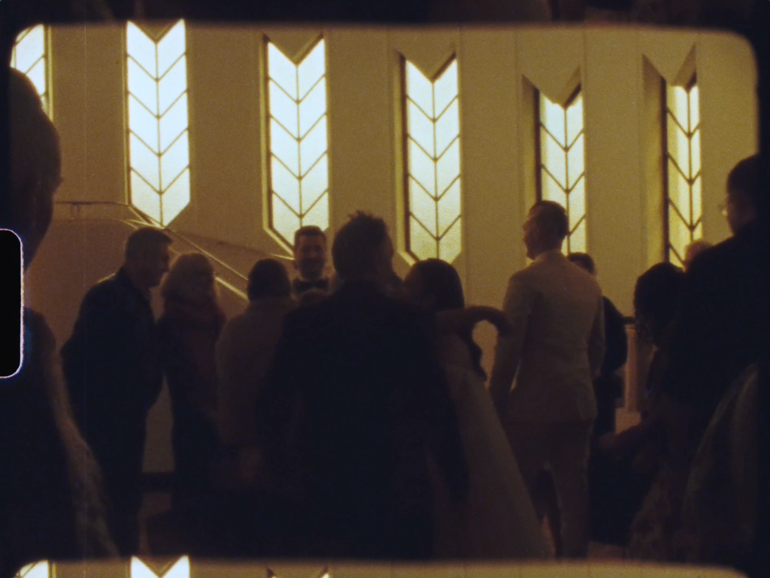 Wedding guests gathered inside a church with glowing arrow-shaped stained glass windows.