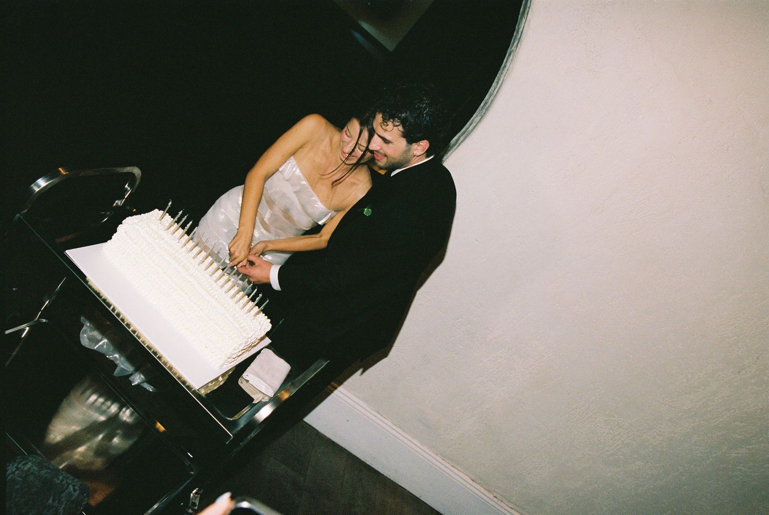 Bride and groom sharing a kiss while cutting their white wedding cake.