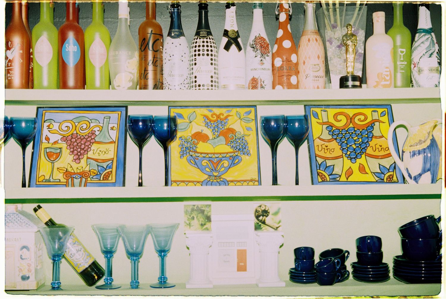 Colorful display shelf with decorative wine bottles, blue stemware, Italian ceramic tiles, and cobalt blue dishware collection.