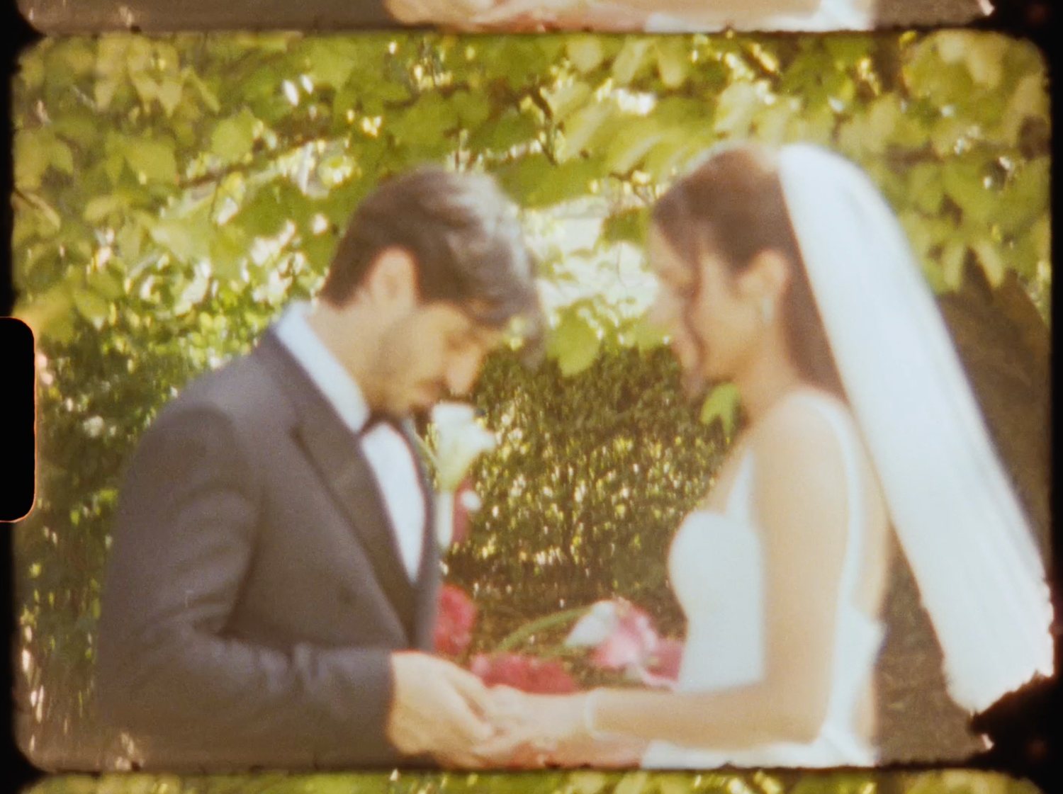 Groom placing wedding ring on bride's finger outdoors surrounded by green foliage in vintage film style.
