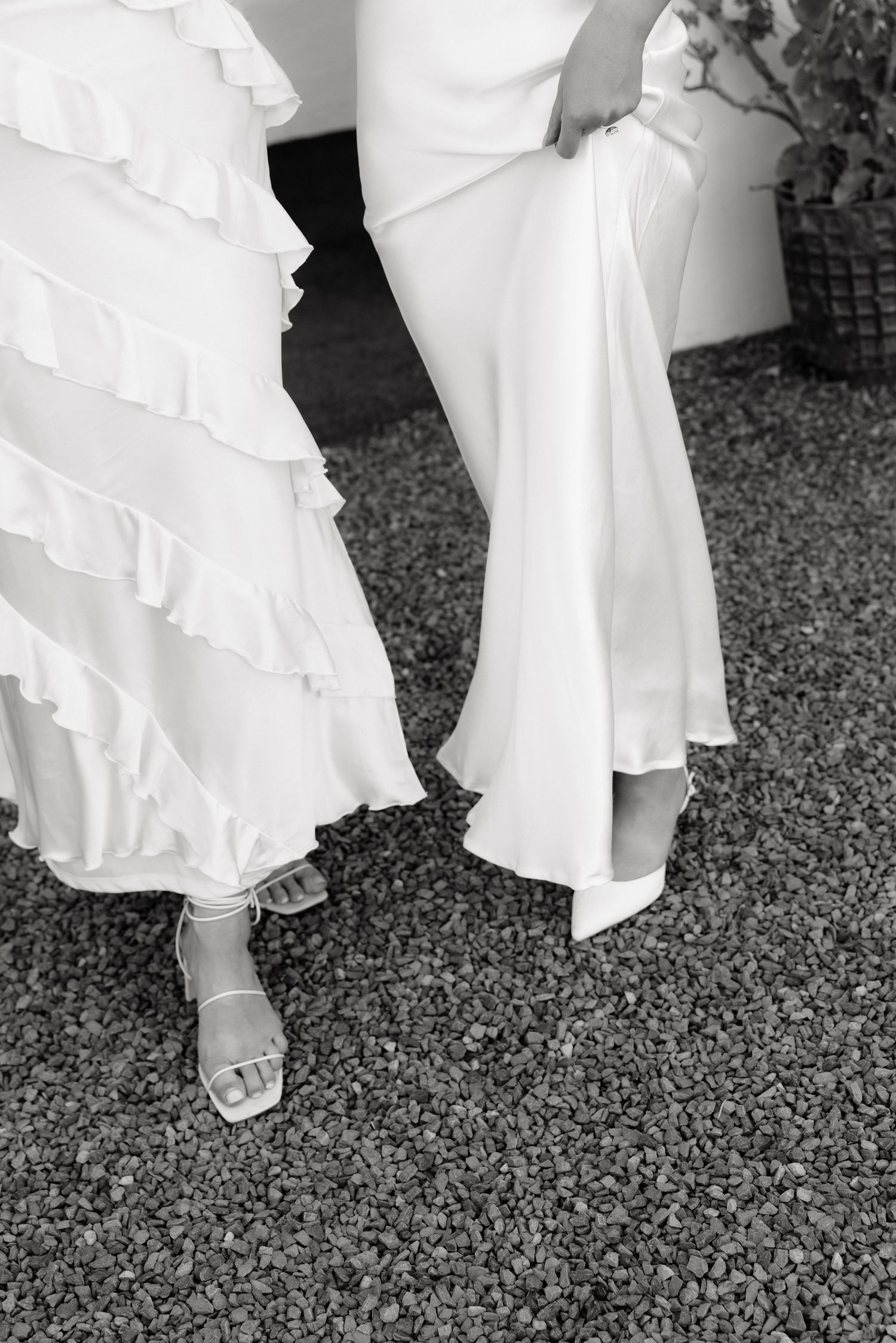 Black and white detail shot of two brides in white wedding dresses and heels.