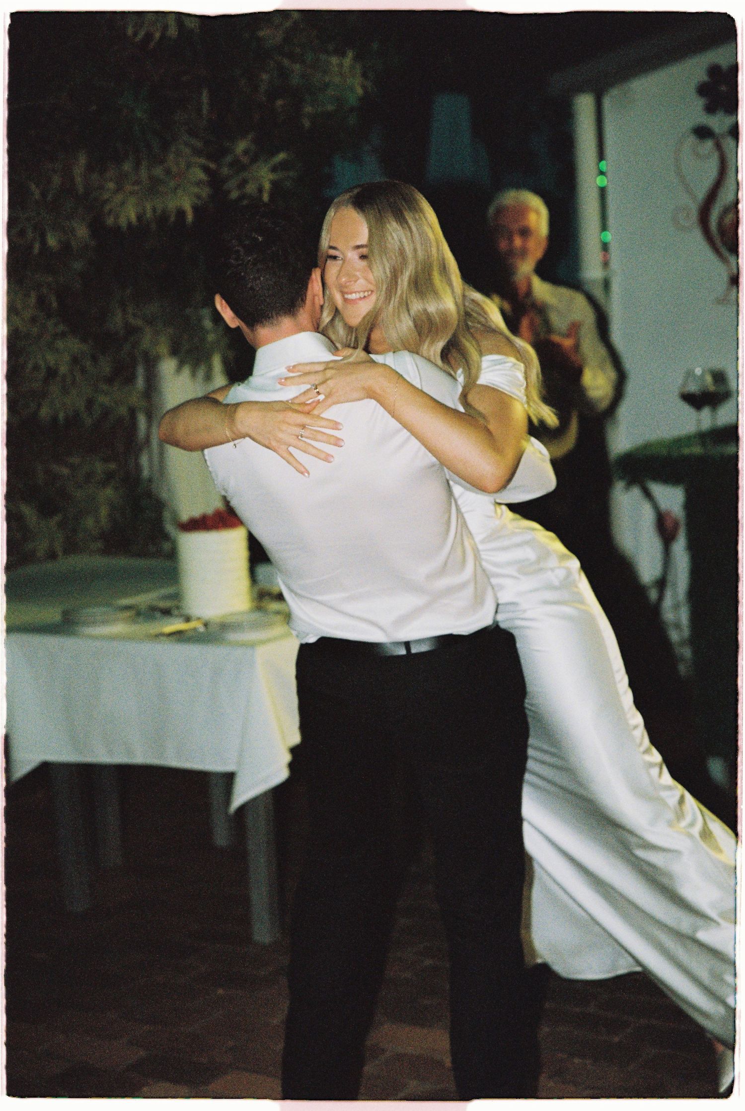 Bride and groom share their first dance at wedding reception, bride smiling in white gown.