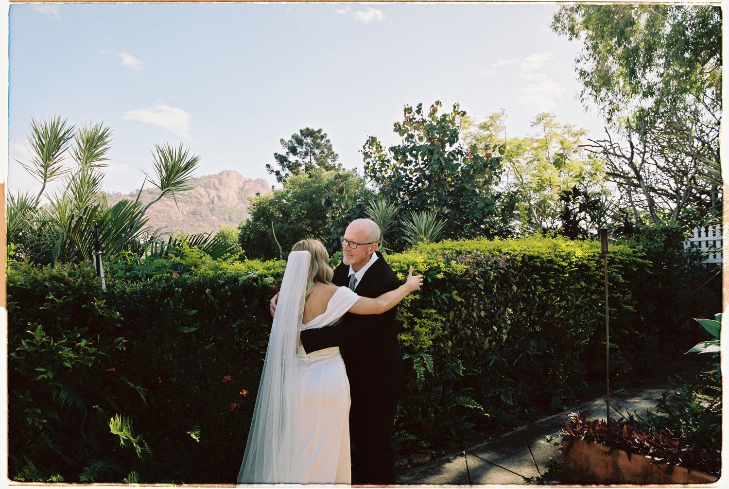 Bride and groom share a romantic first dance in a lush garden with mountain views on their wedding day.