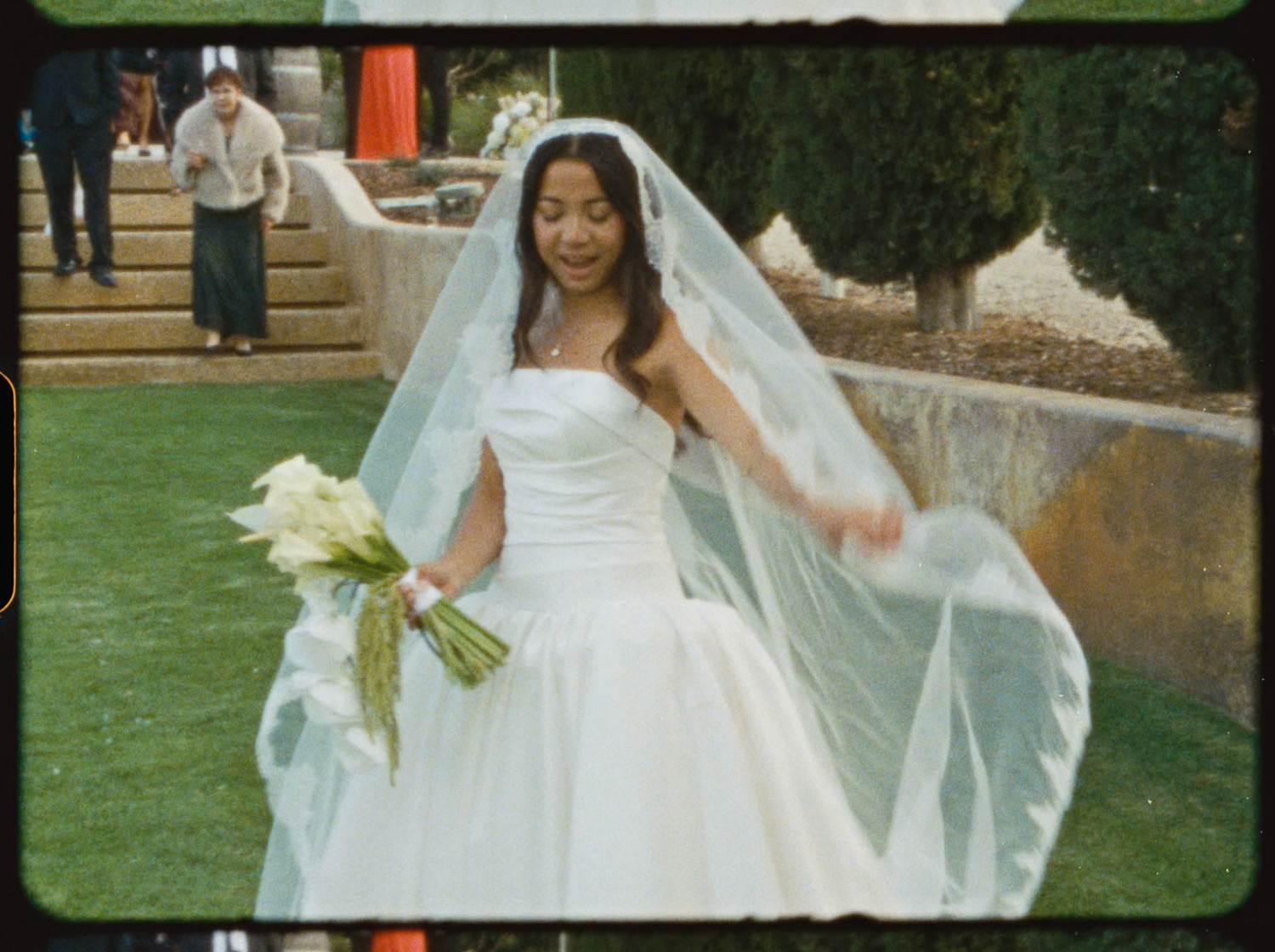 Beautiful Asian bride in strapless white gown and long veil holds white calla lily bouquet outdoors.