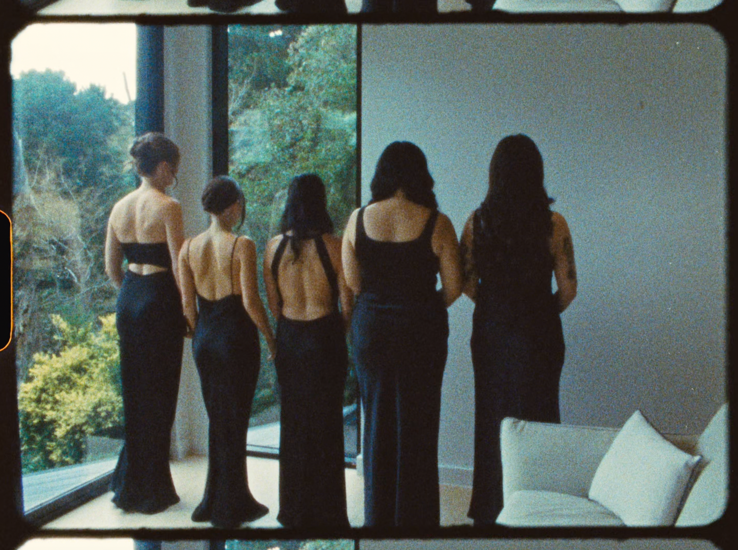 Four bridesmaids in elegant backless black gowns standing with backs to camera near windows.
