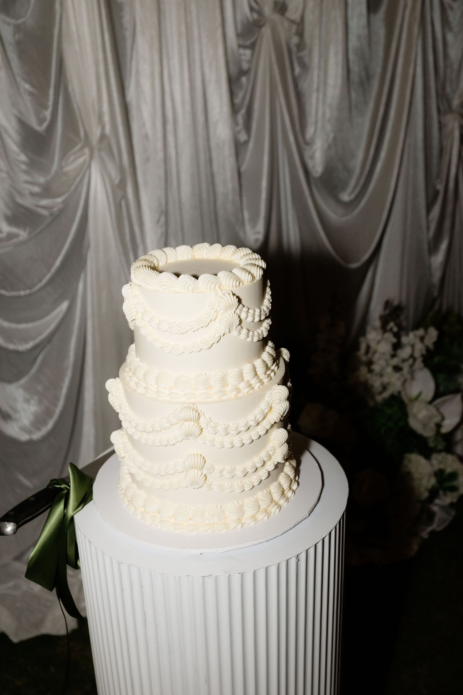 Elegant four-tier white wedding cake with ruffled buttercream details displayed on a white pedestal stand.