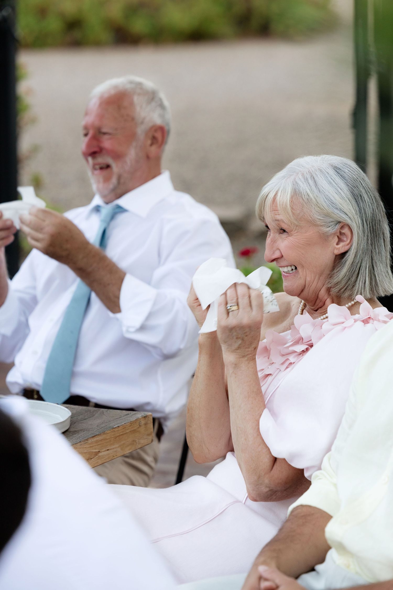 Smiling elderly couple enjoying wedding reception speeches at outdoor dining table.