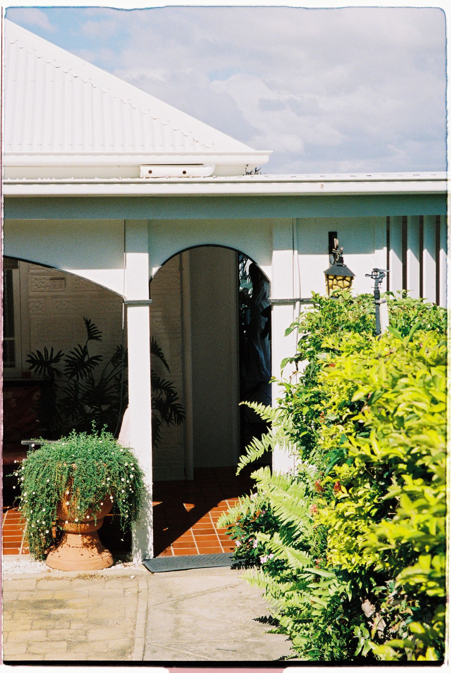 Charming white house exterior with arched veranda, terracotta brick path and tropical garden.