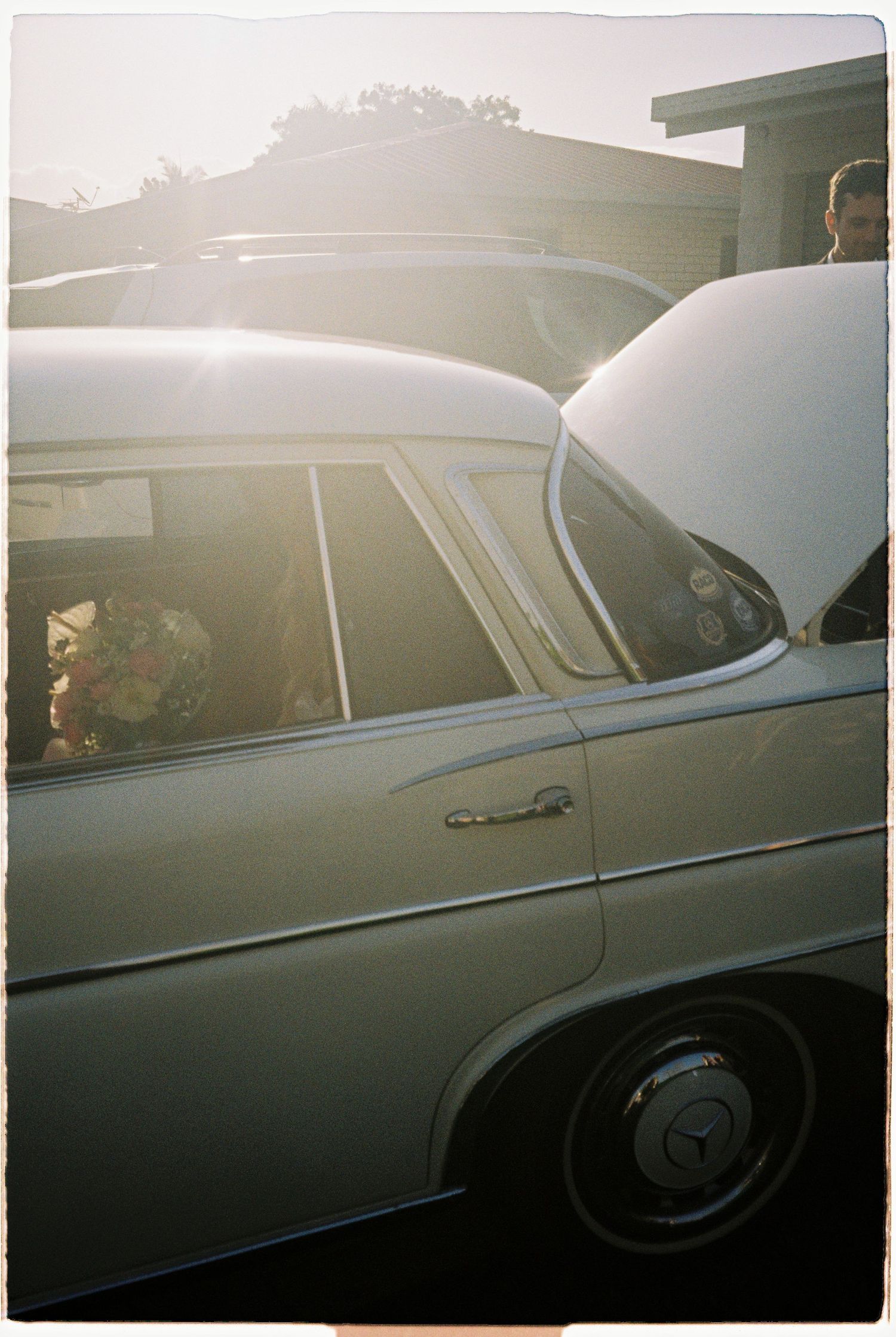 Sunlit vintage white Mercedes-Benz wedding car with bride visible through window.