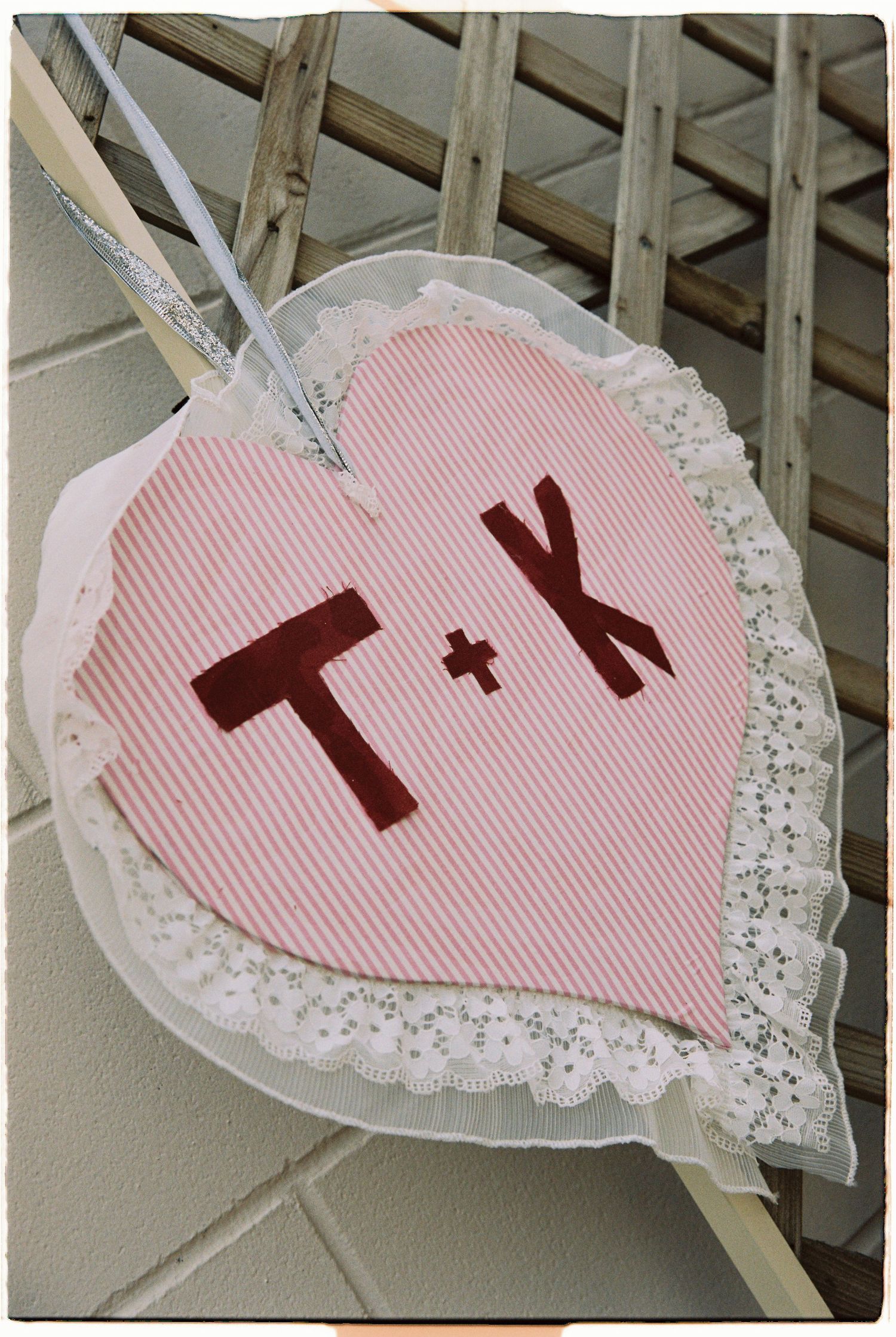 Handmade pink striped fabric heart decoration with lace trim displaying initials T and K for a wedding.