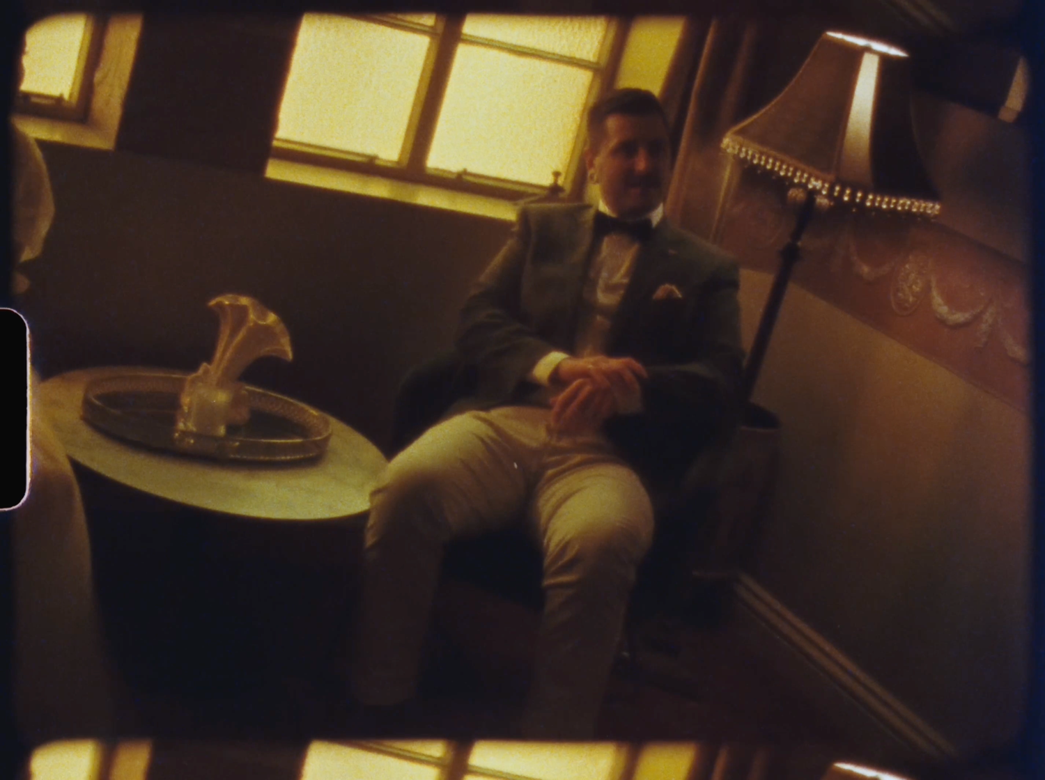 Elegant man in tuxedo relaxing in vintage train compartment with warm golden lighting and ornate decor.