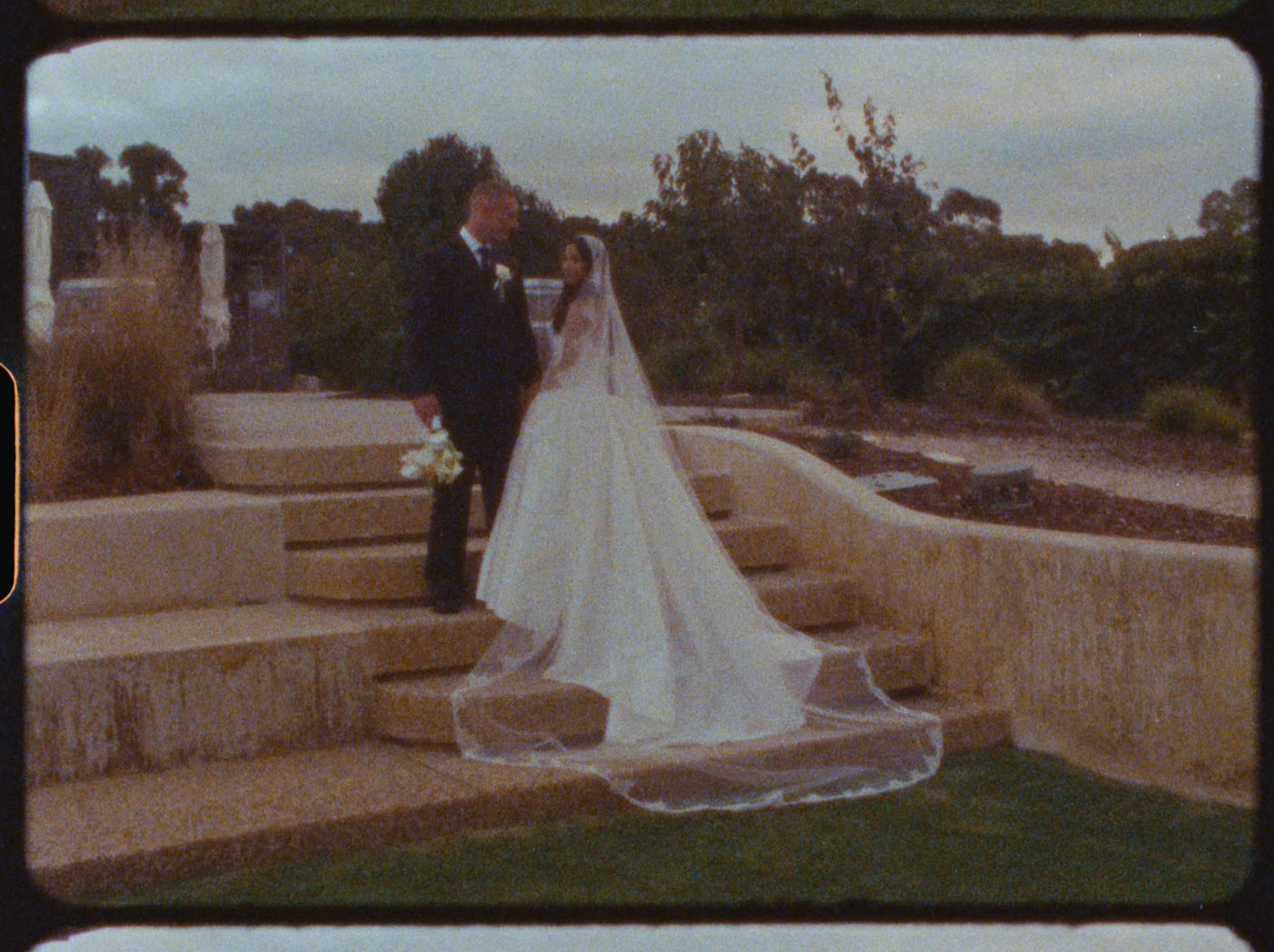 Bride and groom stand on stone steps in a garden during their outdoor wedding ceremony.