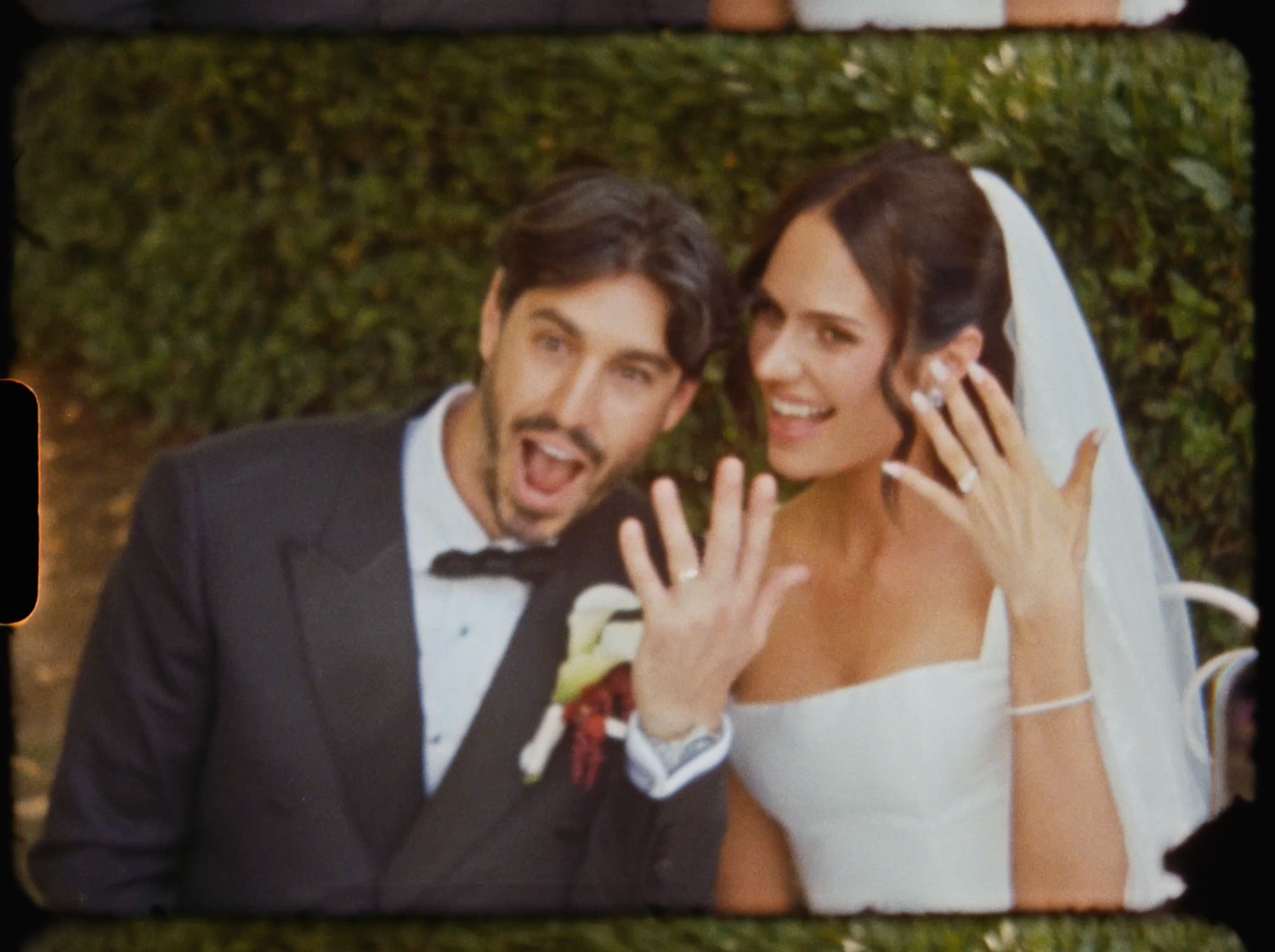 Newlyweds joyfully show off their wedding rings while posing together outdoors after their ceremony.