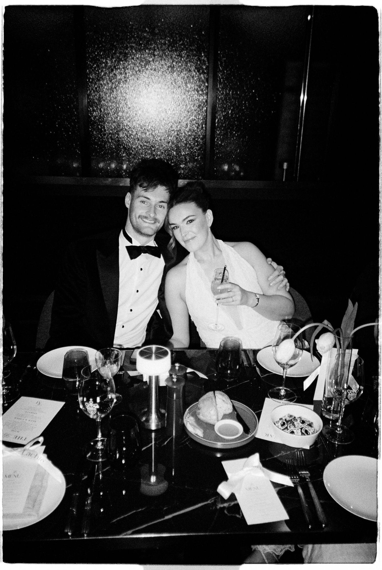 Couple in formal wedding attire smiling together at elegant candlelit dinner reception table.