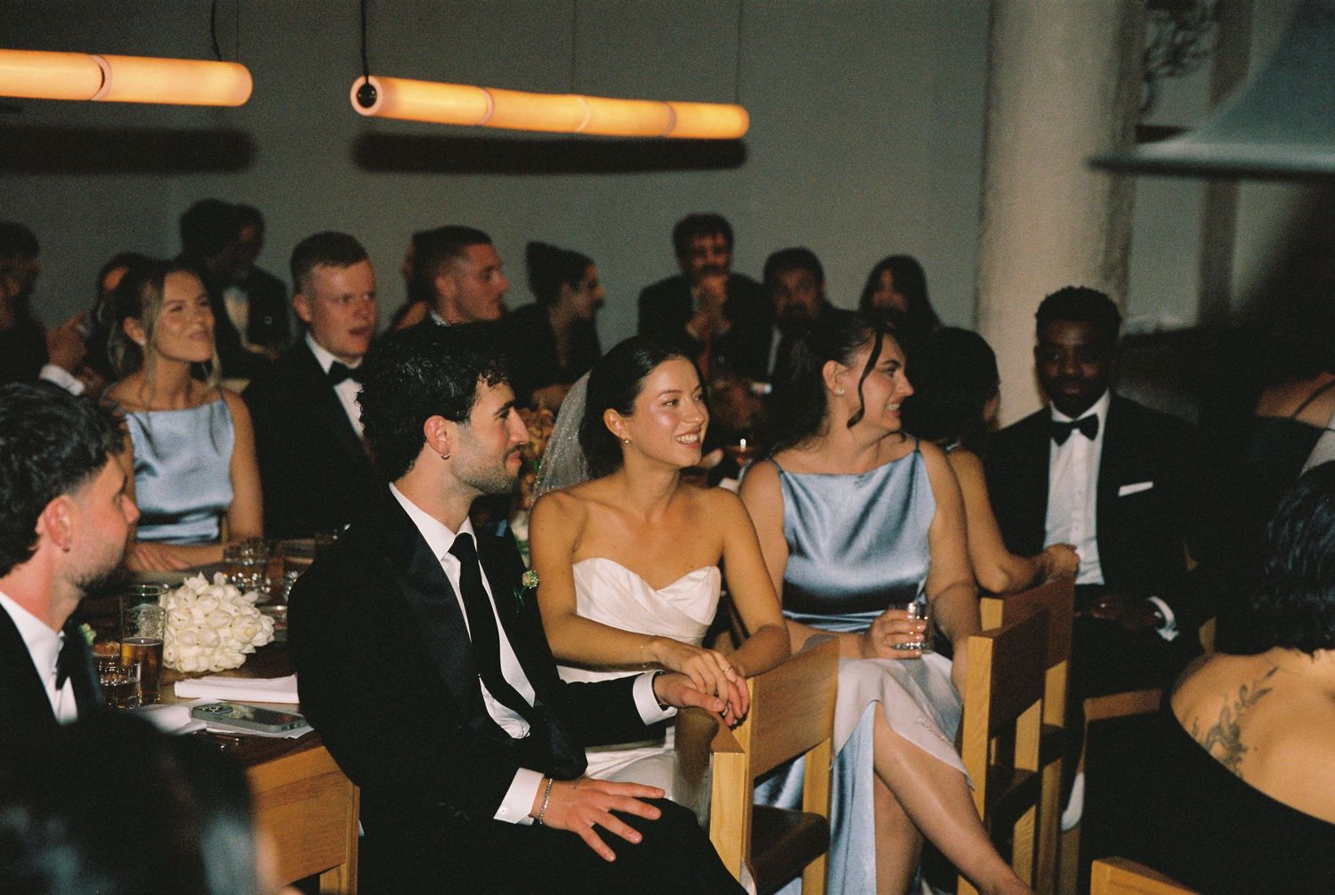 Bride and groom seated with wedding guests in light blue bridesmaid dresses at reception dinner.