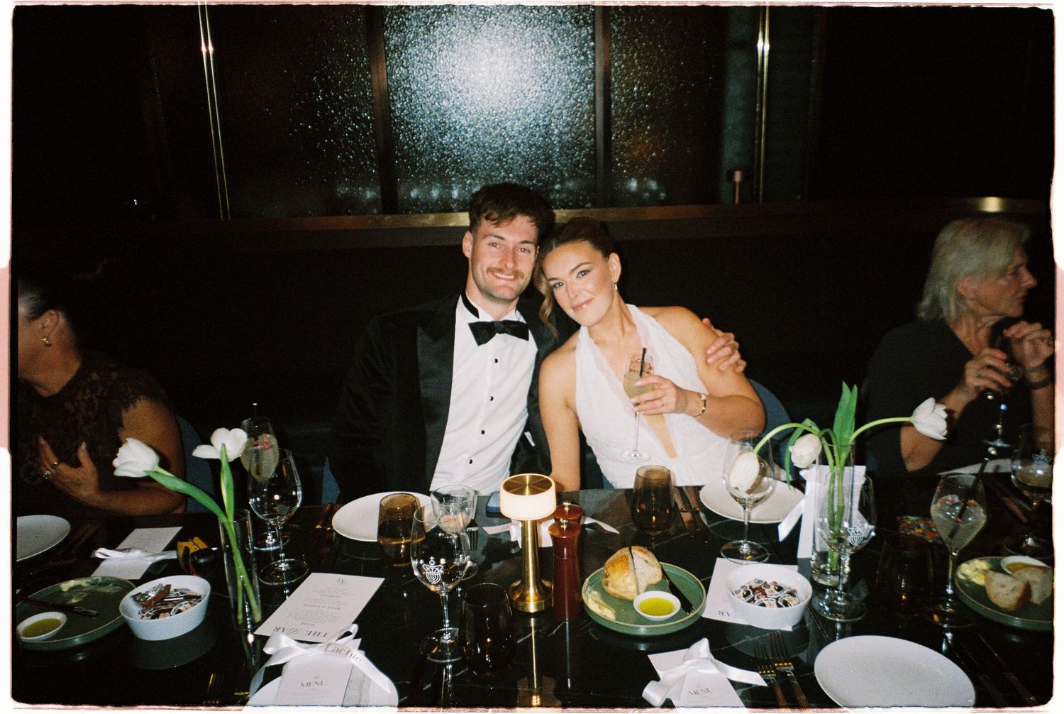 Bride and groom smile together at elegant candlelit wedding reception dinner.