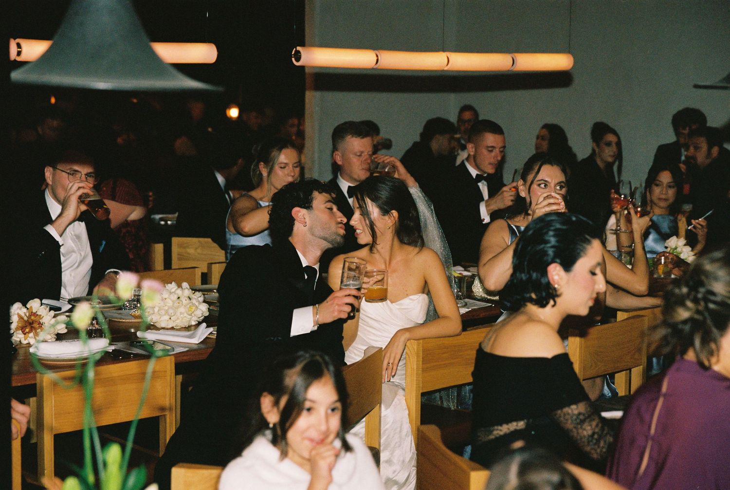 Wedding guests in formal attire enjoy drinks and conversation at a seated reception dinner.