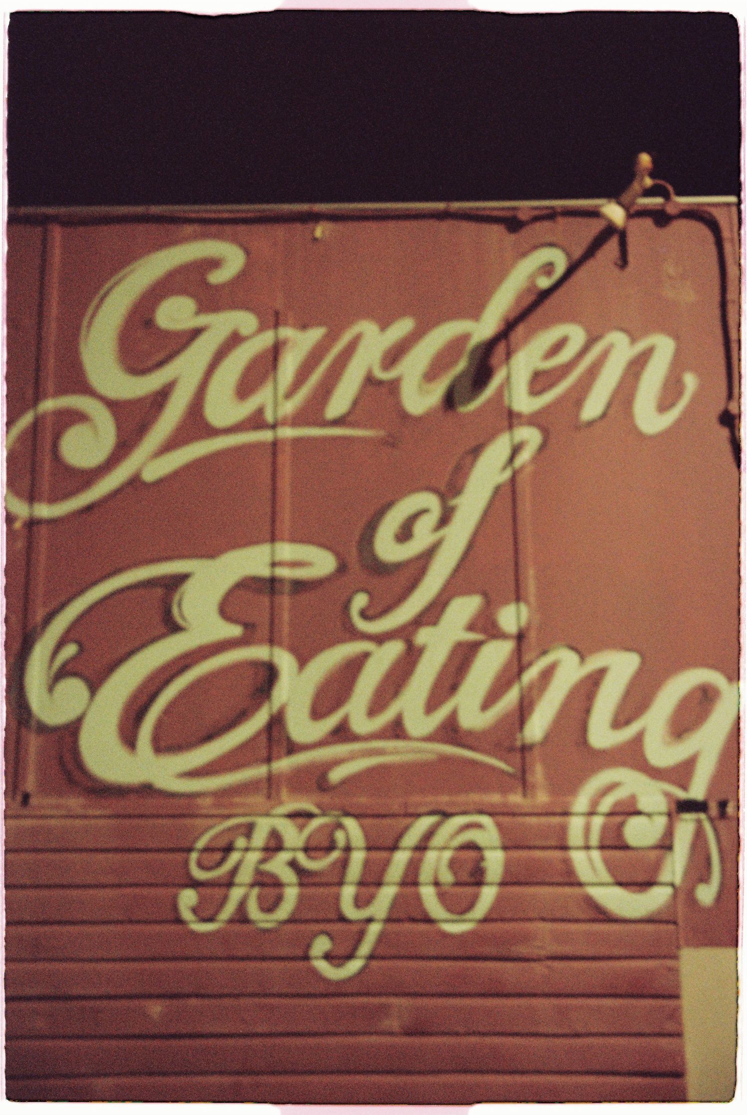 Vintage red sign reading Garden of Eating BYO on a wooden wall at night.