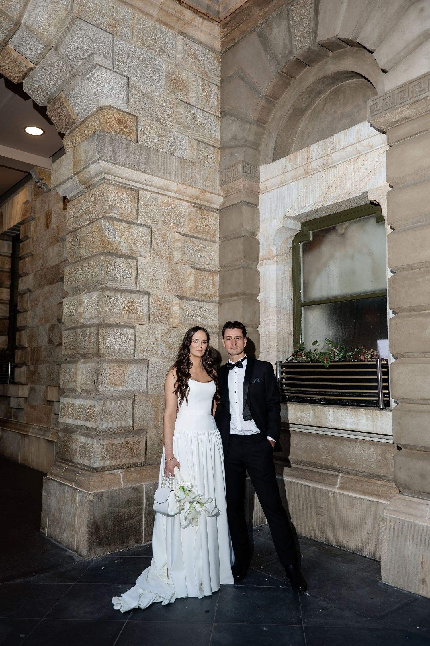 Elegant bride and groom posing beside sandstone columns of a historic building.