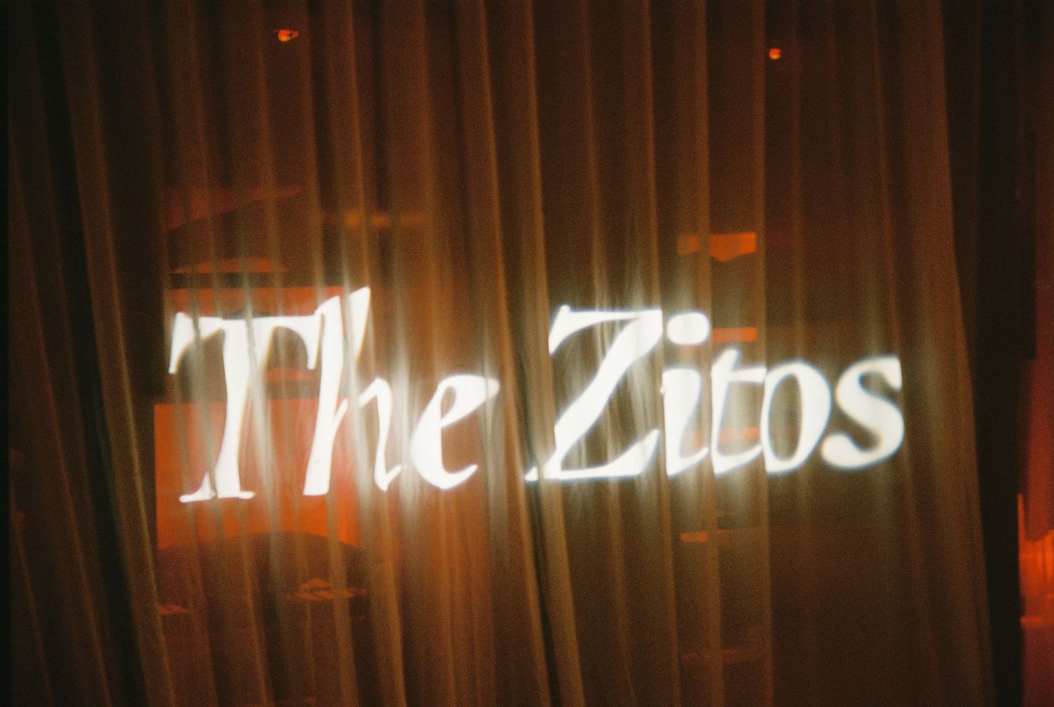 Elegant illuminated sign reading The Zitos displayed against warm golden curtain backdrop at wedding.