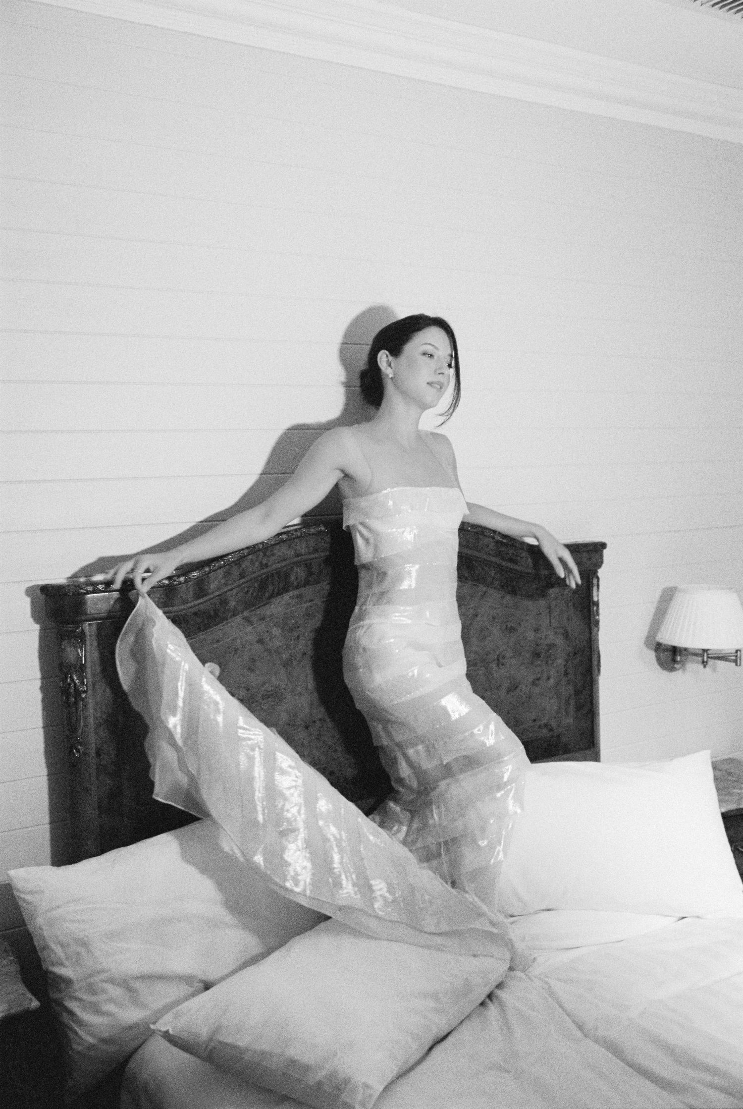 Bride in strapless wedding gown posing gracefully on bed in hotel room.