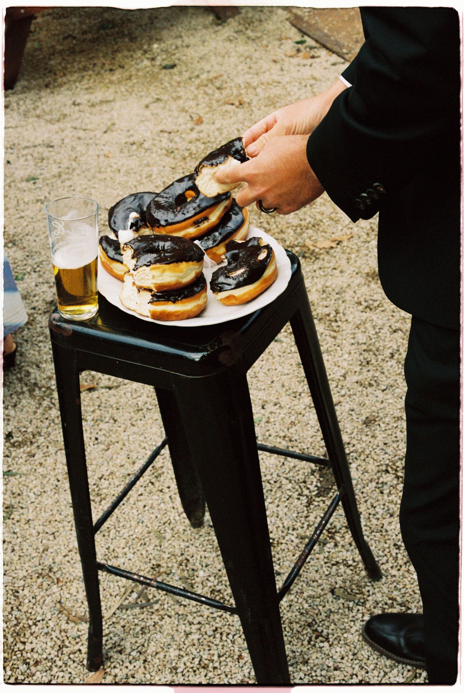 Person in suit picking up a burger from a plate of sliders on a black metal stool outdoors.