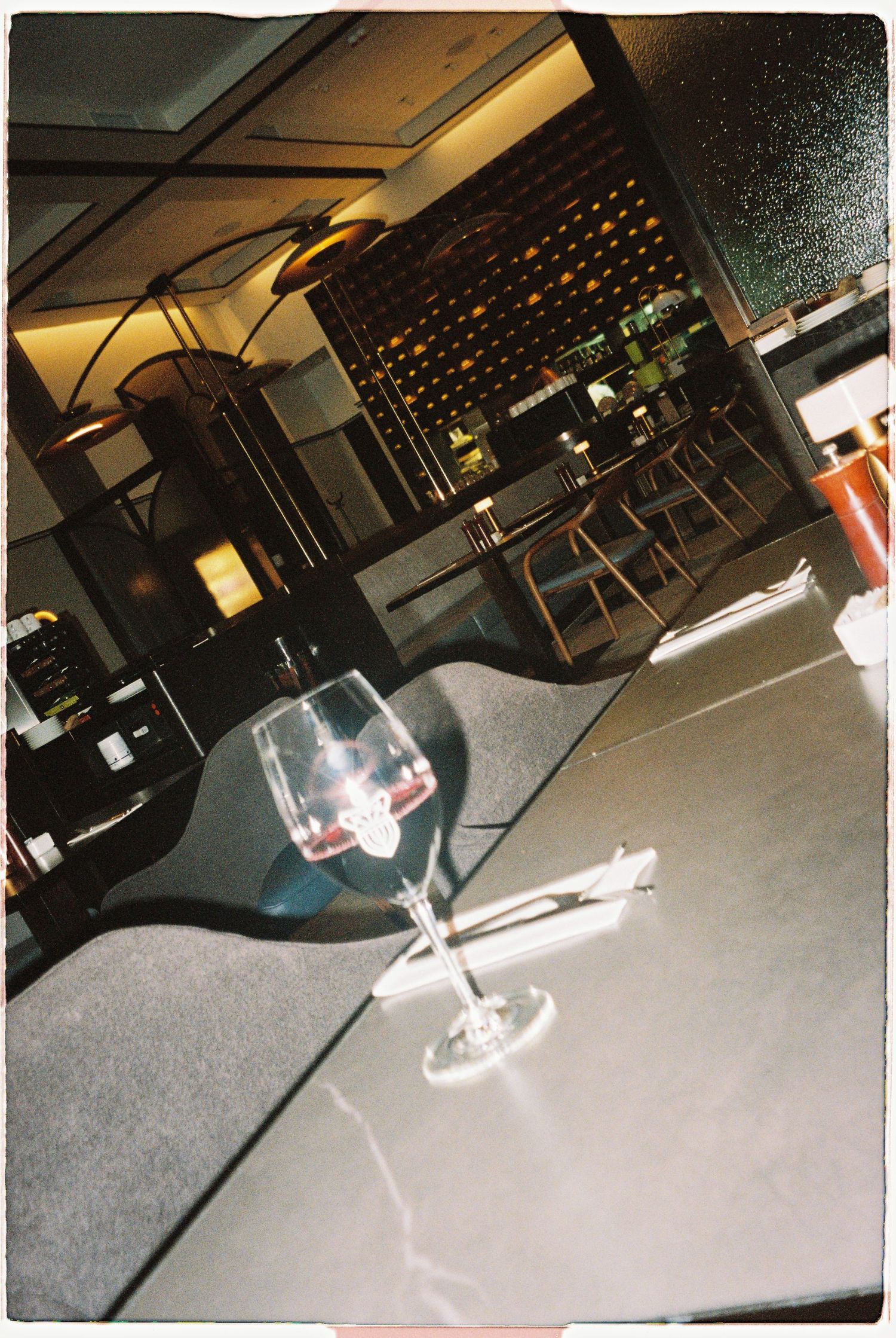 A wine glass with red wine on a dark table in an upscale restaurant with a wine rack in the background.
