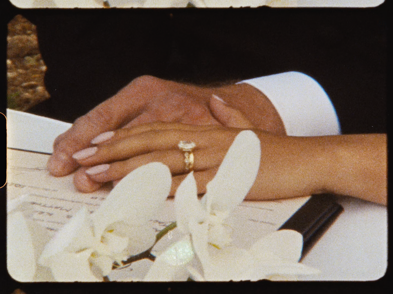 Close-up of bride and grooms hands with wedding ring resting on ceremony documents with white orchids.