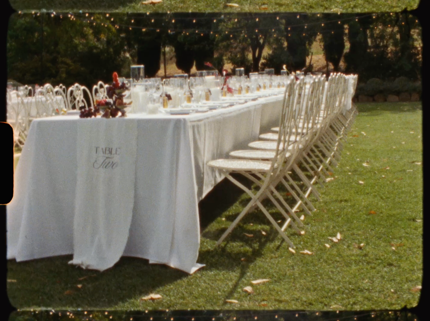 Outdoor wedding reception long table with white linen, string lights overhead, and elegant place settings.
