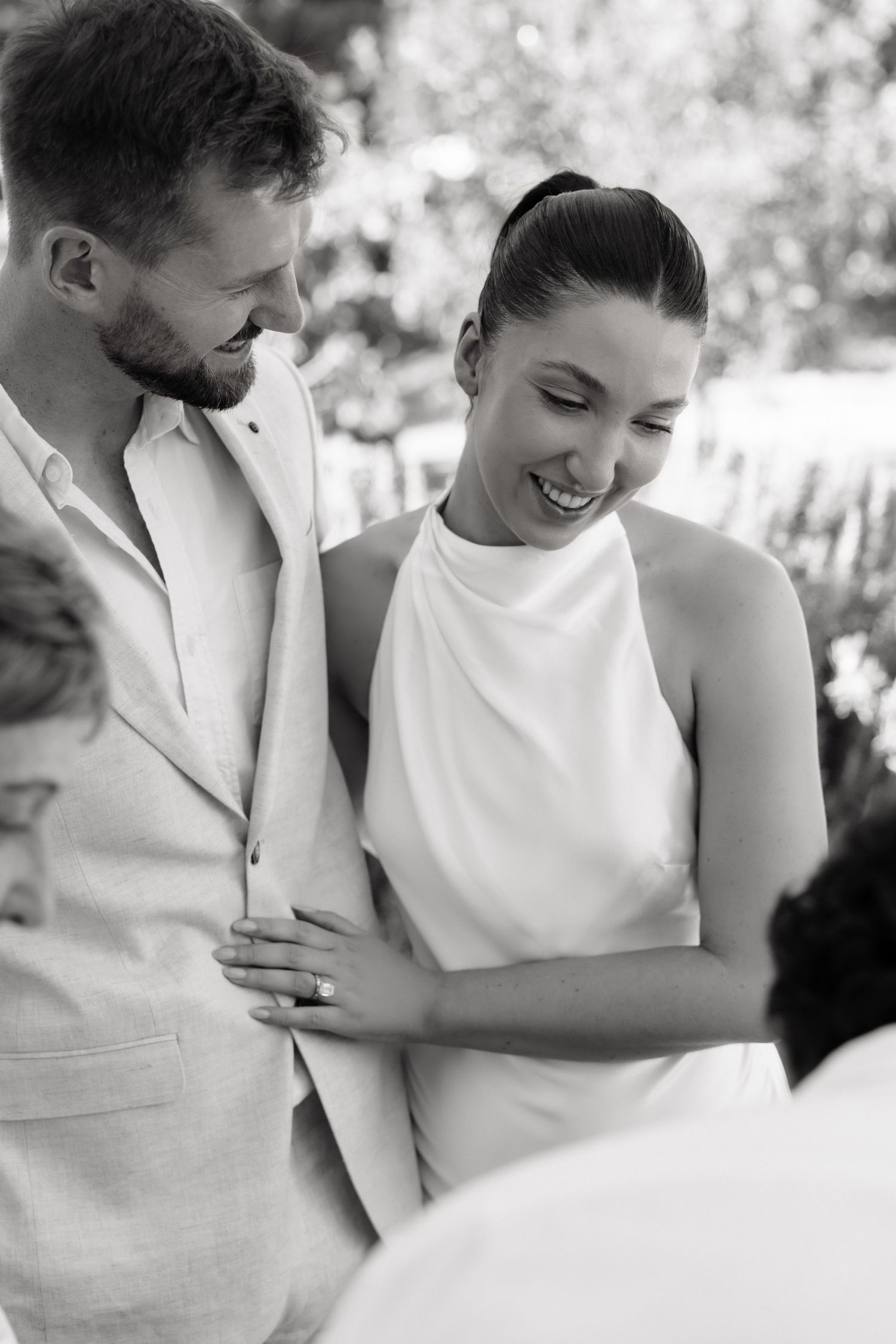 Happy bride in white halter dress laughing with groom in linen suit during outdoor wedding ceremony.