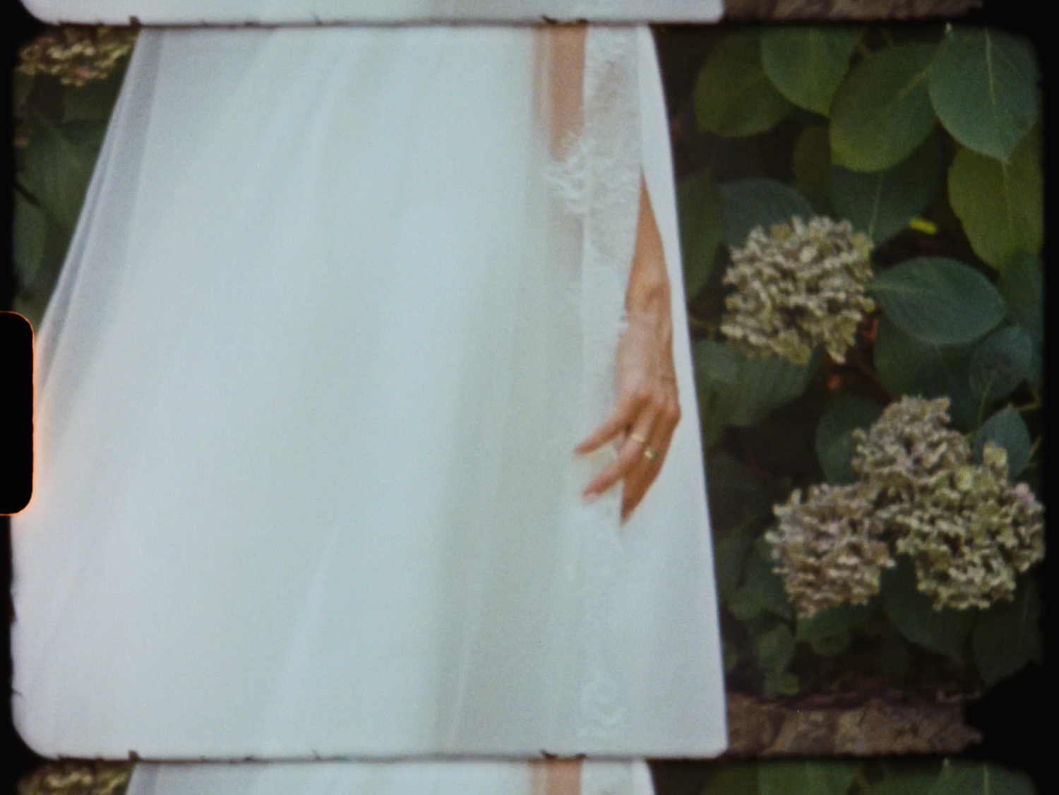 Close-up of a bride's hand in a white lace wedding gown beside blooming hydrangea flowers.