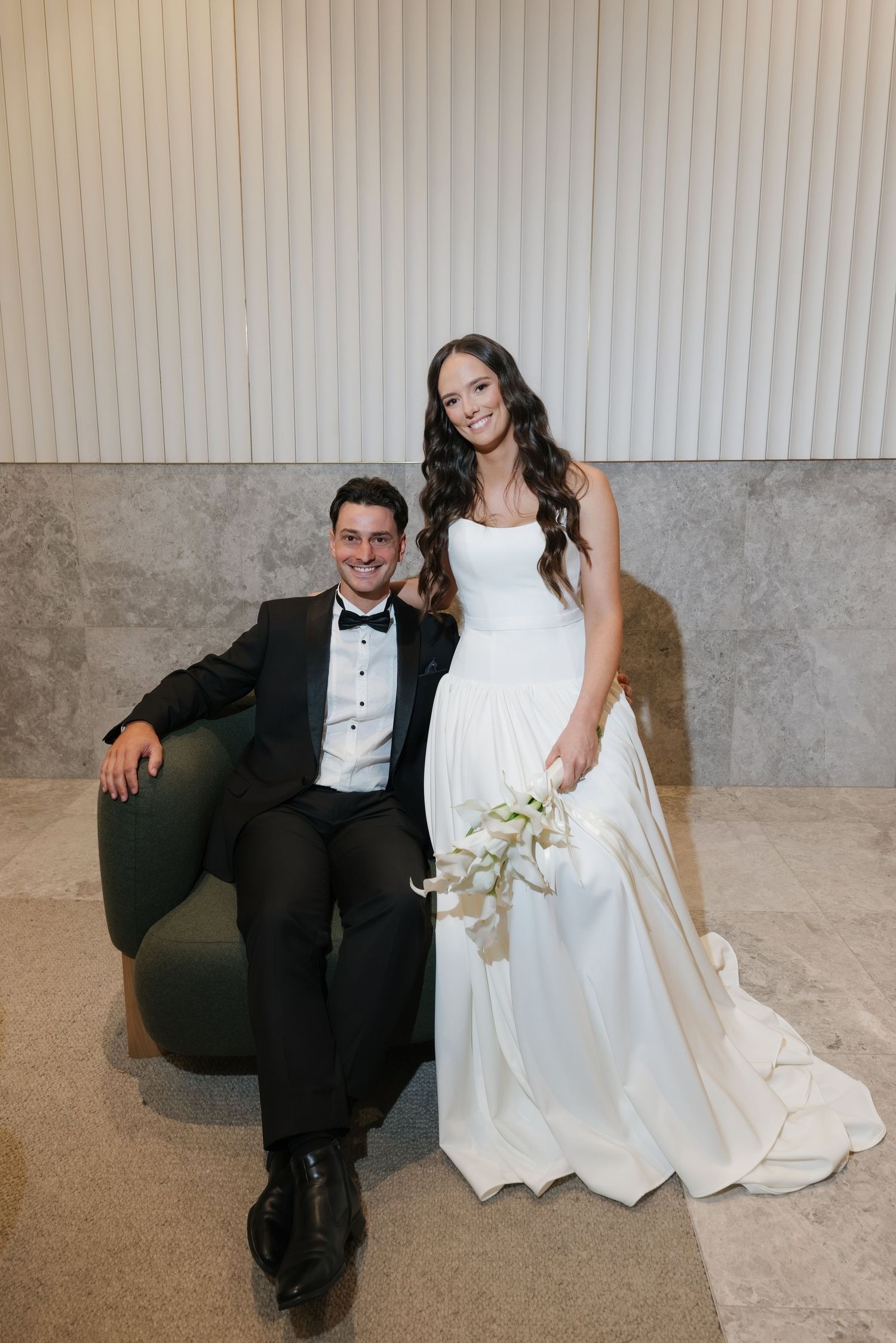 Black and white photo of bride and groom relaxing by fireplace, bride in white gown, groom in tuxedo.