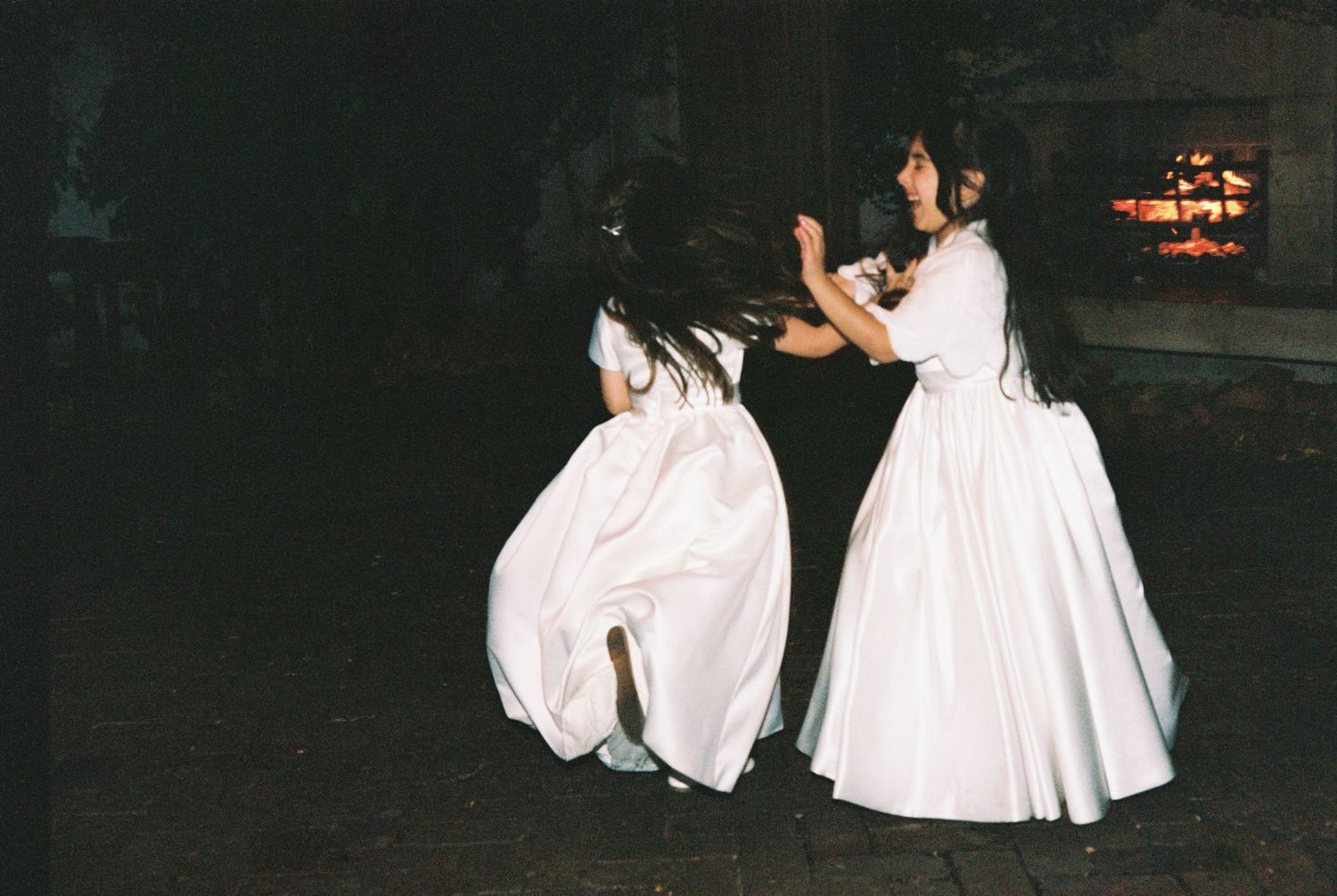 Two flower girls in white dresses twirling and dancing joyfully at a wedding reception.