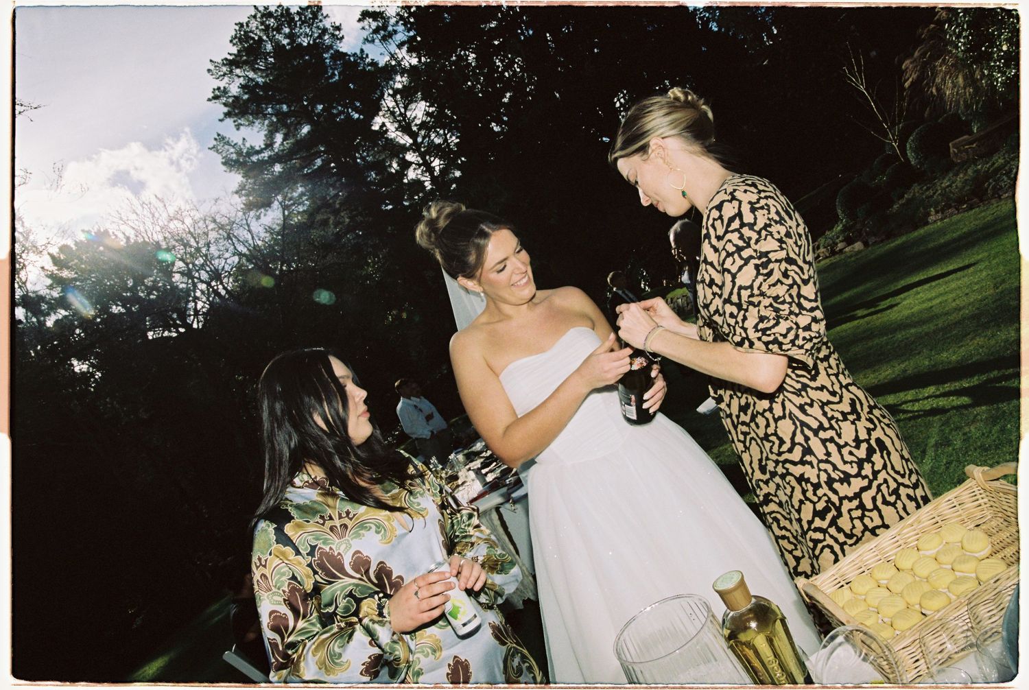 Bride in white strapless gown receives a gift from a guest during outdoor wedding celebration.