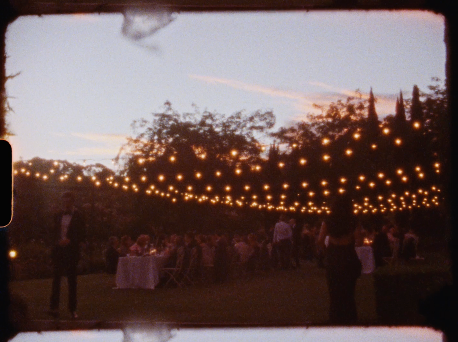 Outdoor wedding reception under canopy of warm string lights at twilight.