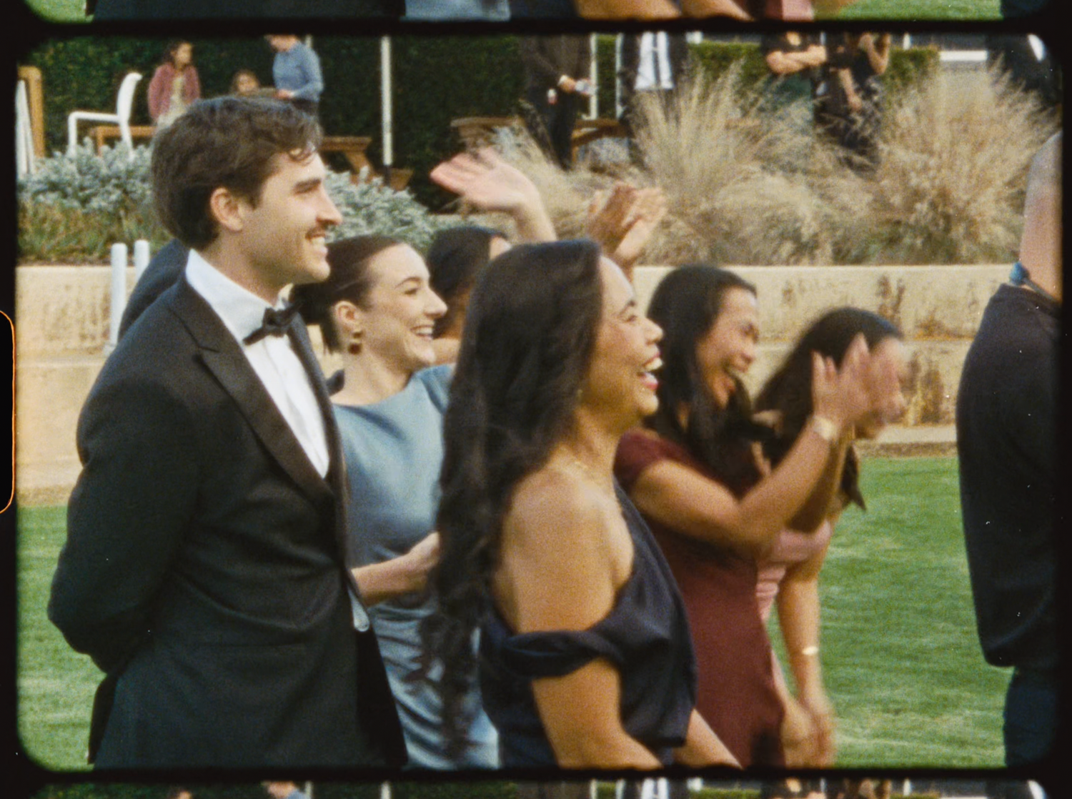 Smiling wedding guests in formal attire celebrating outdoors at a garden wedding reception.