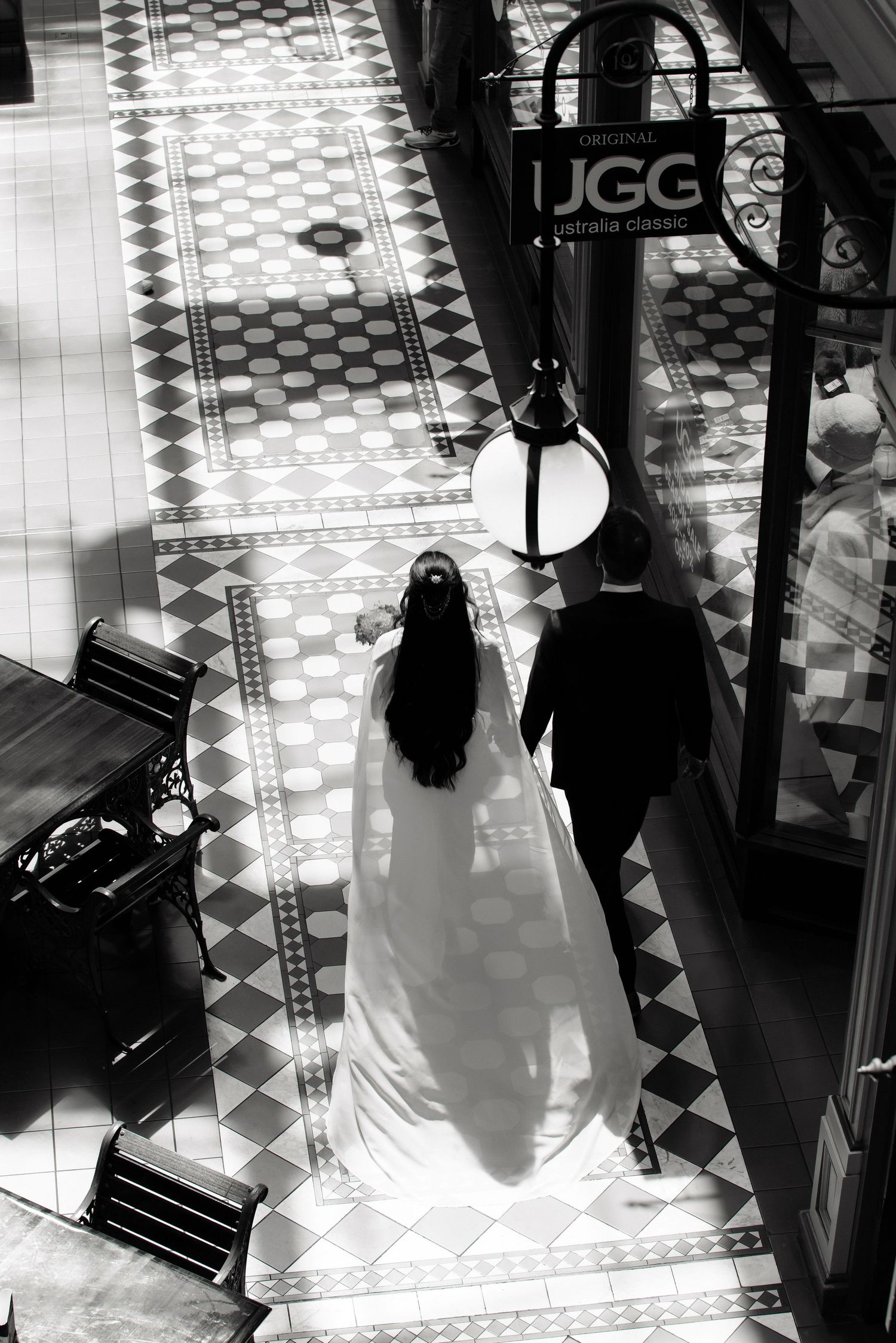 Aerial black and white view of bride and groom walking on ornate tiled floor indoors.