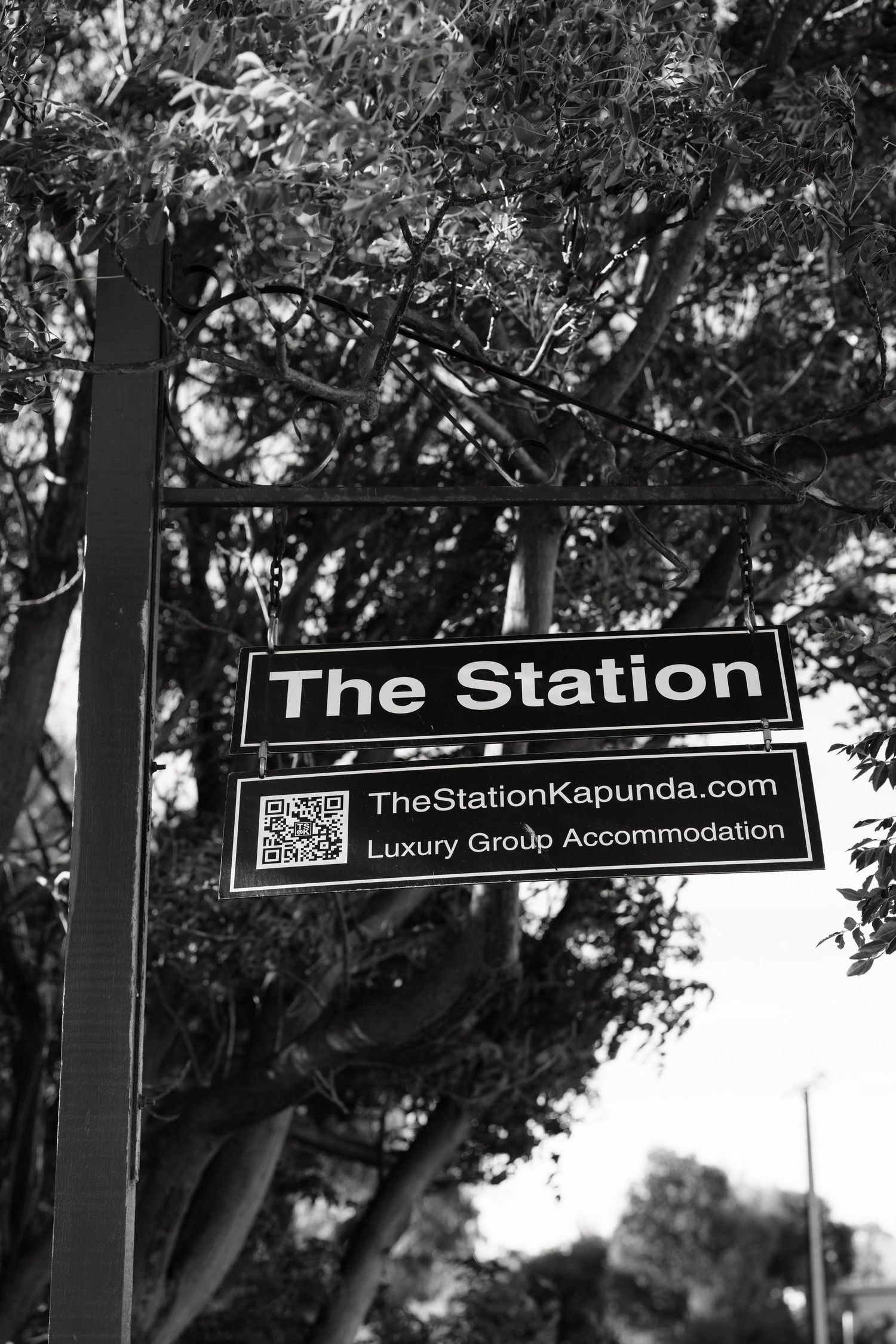 Black and white sign for The Station Kapunda luxury group accommodation surrounded by trees.