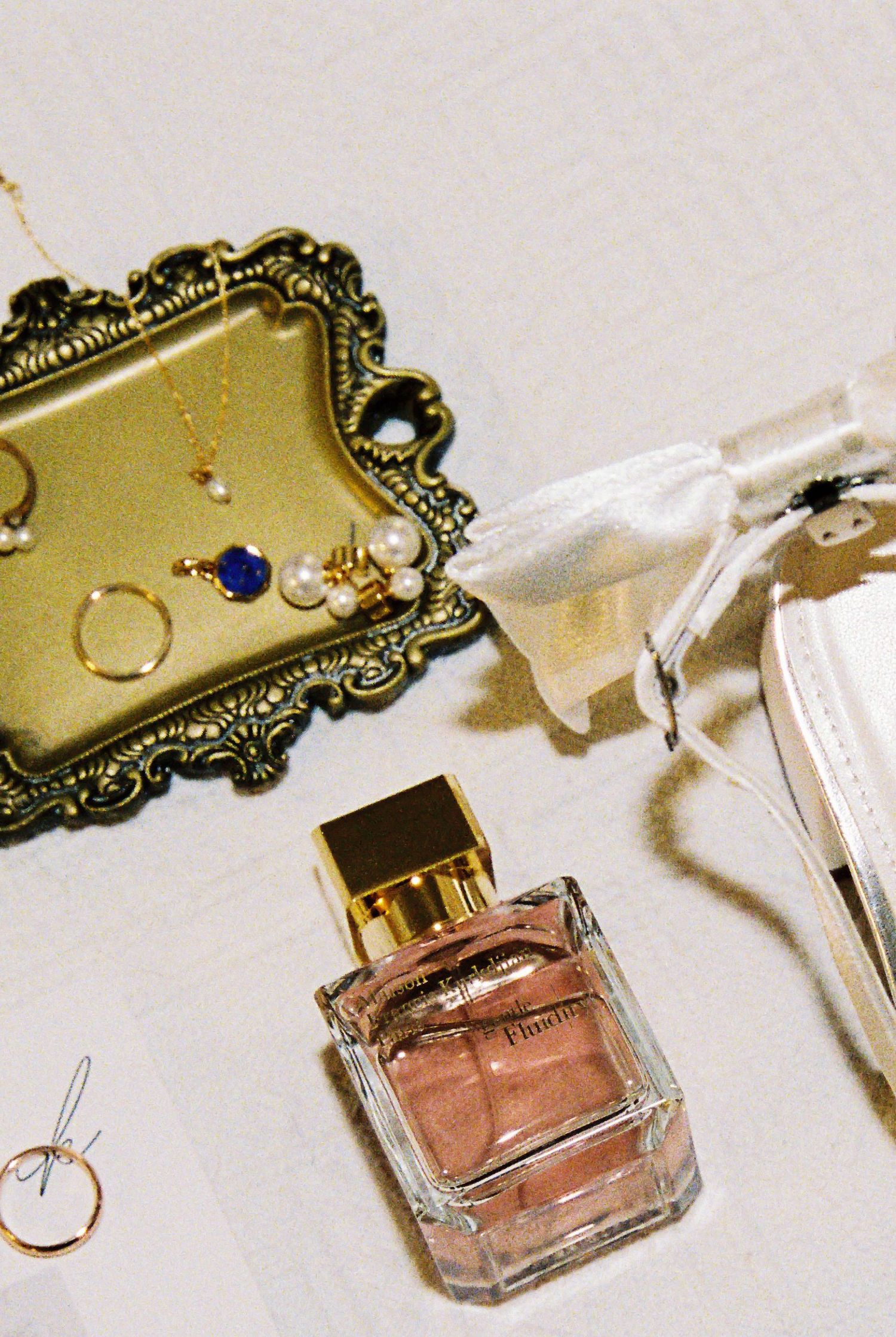 Flat lay of wedding accessories including perfume, gold jewelry tray, and white bridal bag.