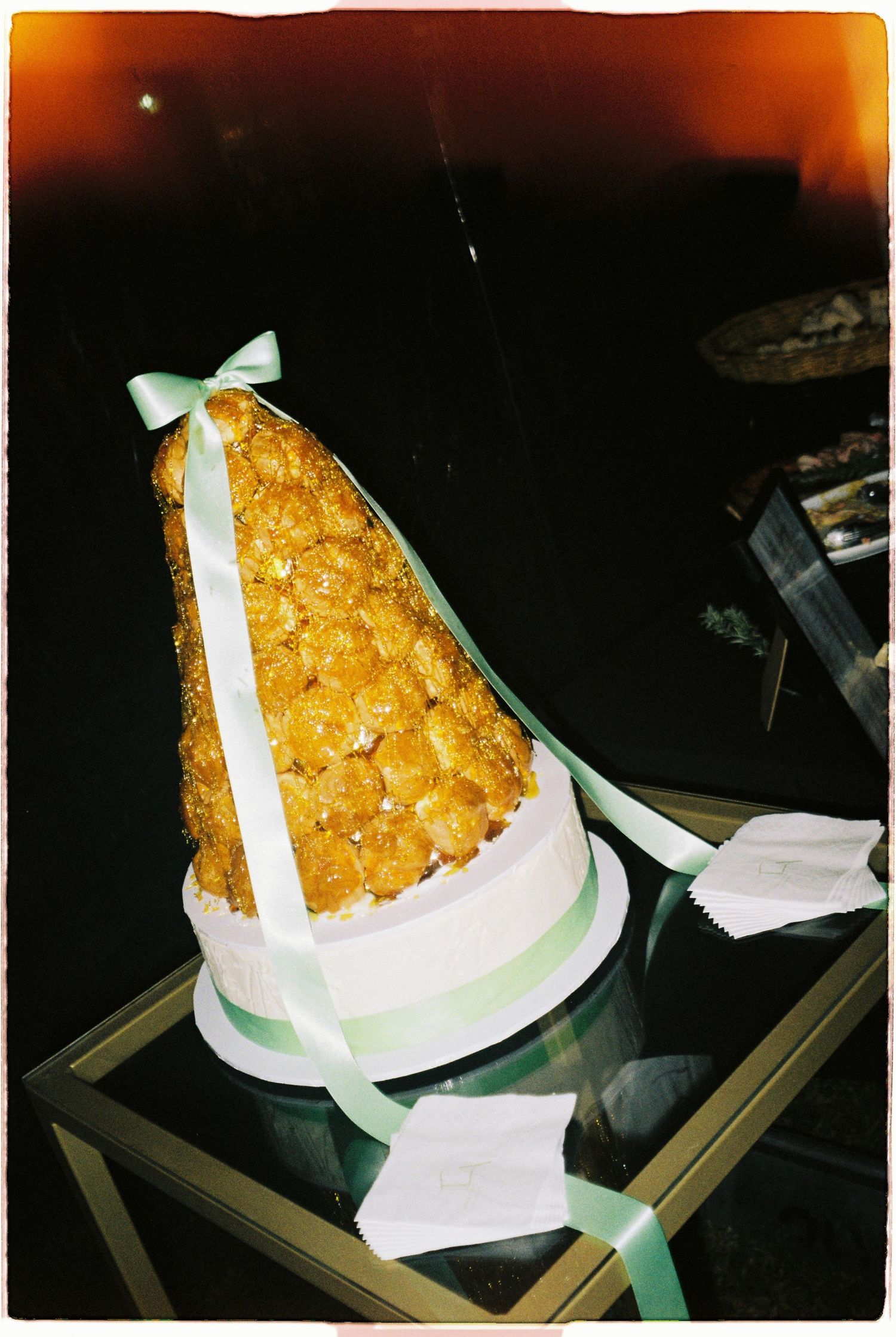 Elegant croquembouche wedding cake tower decorated with green ribbons and bow on a glass table.