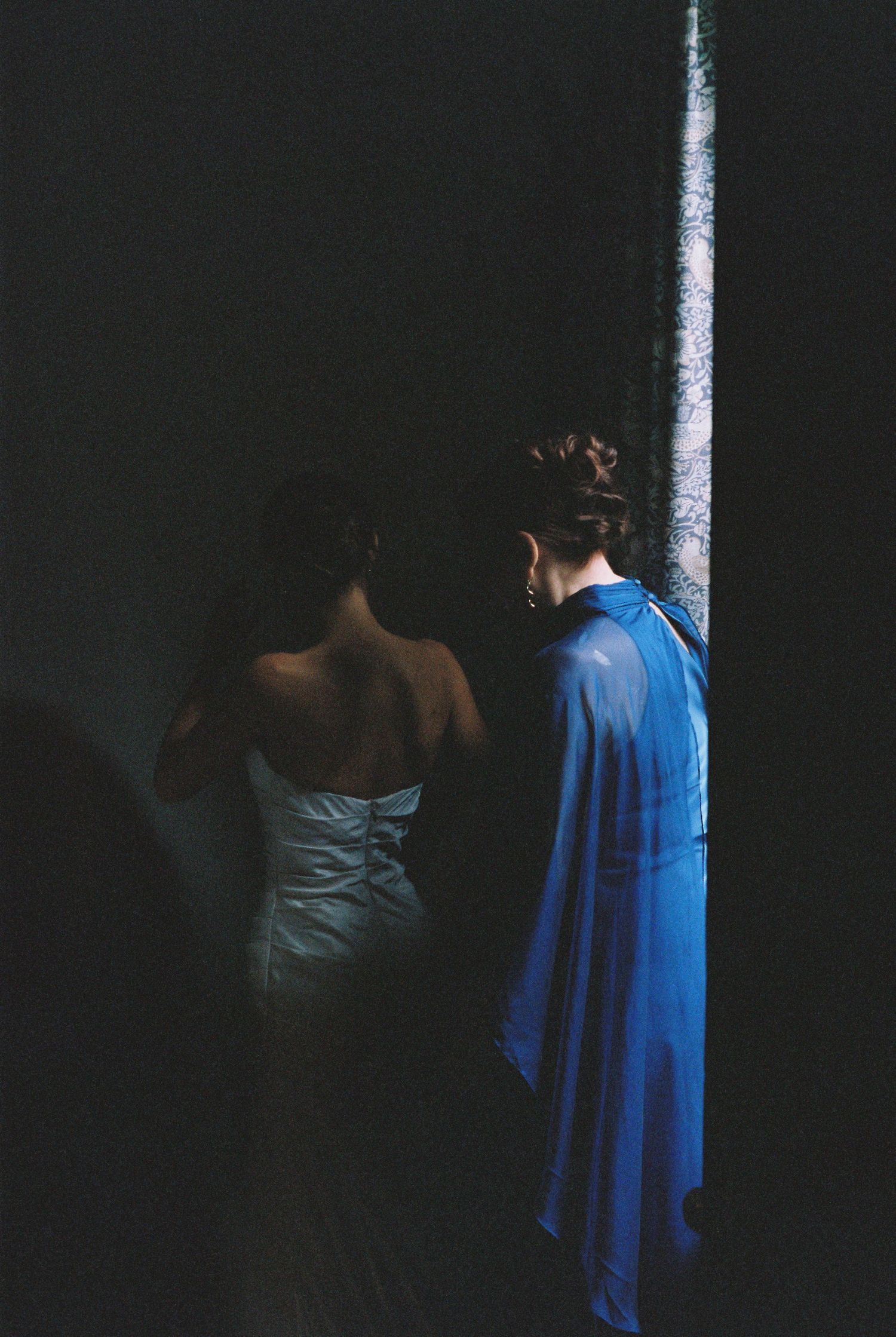 Bride in strapless white gown standing in dramatic dark shadow beside a streak of blue light.