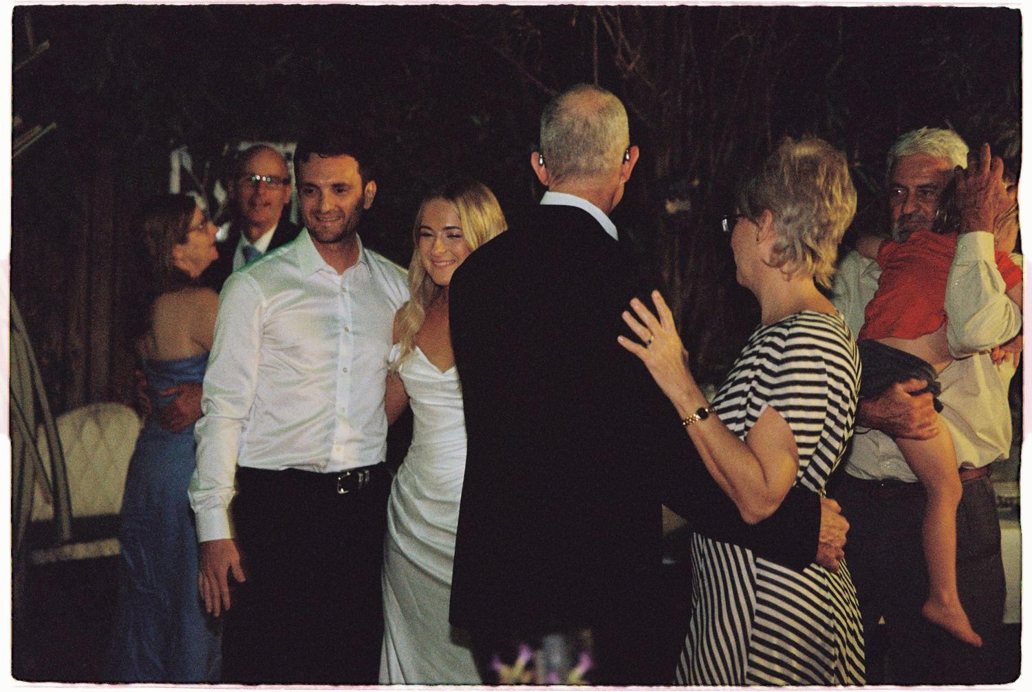 Guests dancing and celebrating at an outdoor wedding reception, with bride and groom smiling joyfully.
