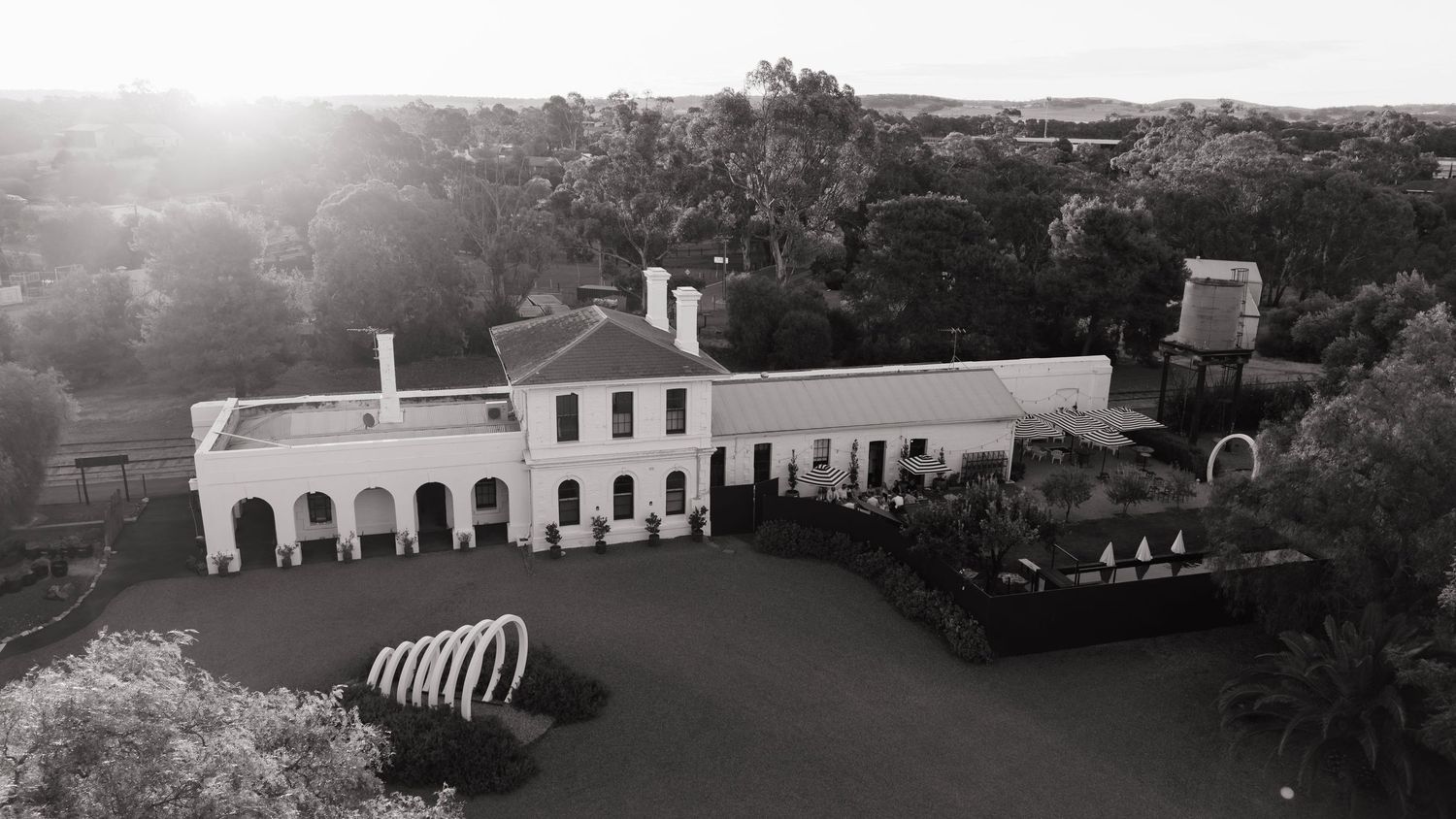 Black and white aerial view of elegant white colonial wedding venue surrounded by trees.