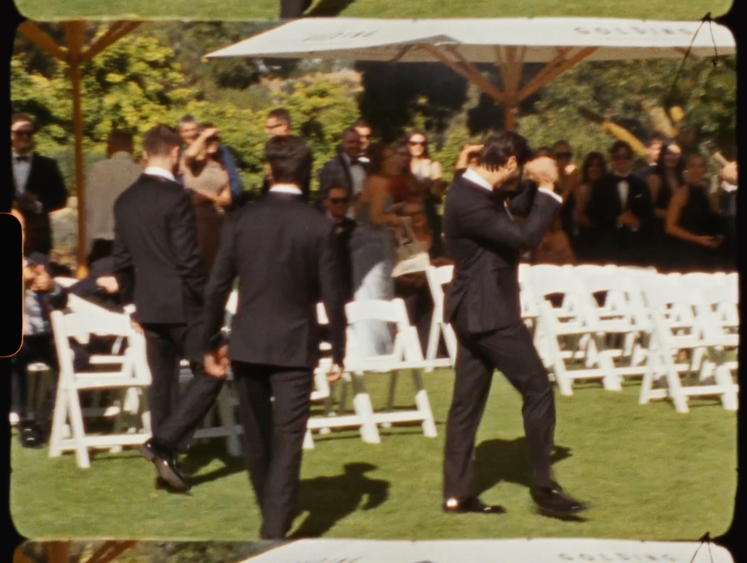 Groomsmen in black tuxedos escorting guests down the aisle at outdoor wedding ceremony.