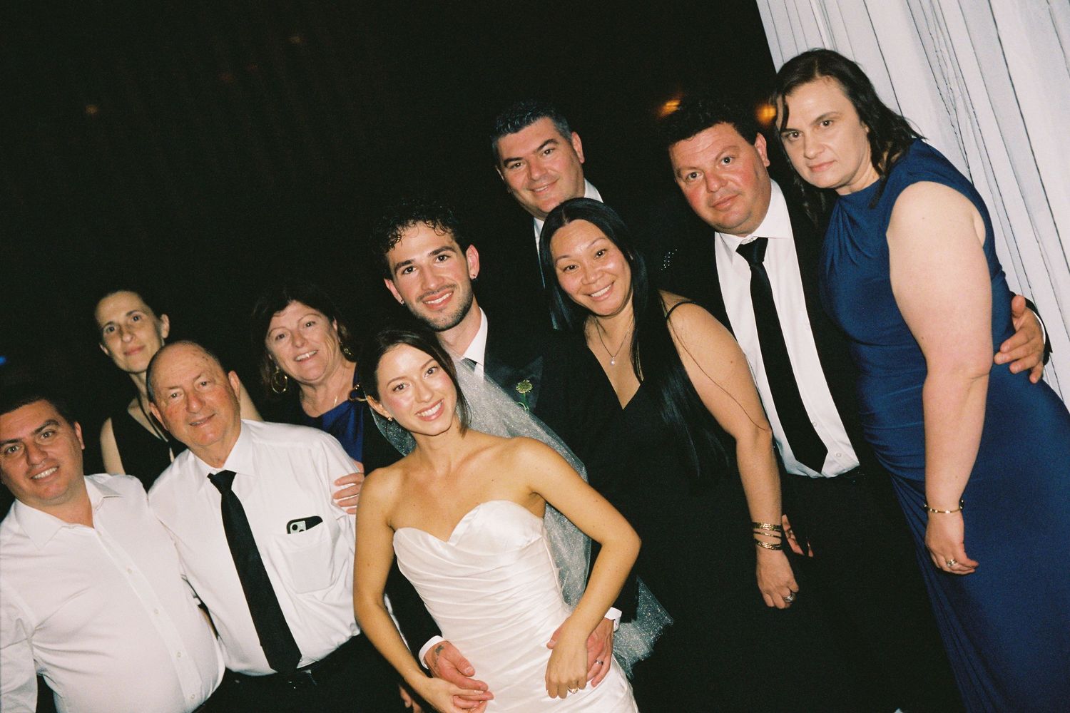 Bride and groom pose with family and friends for a group photo at their wedding reception.